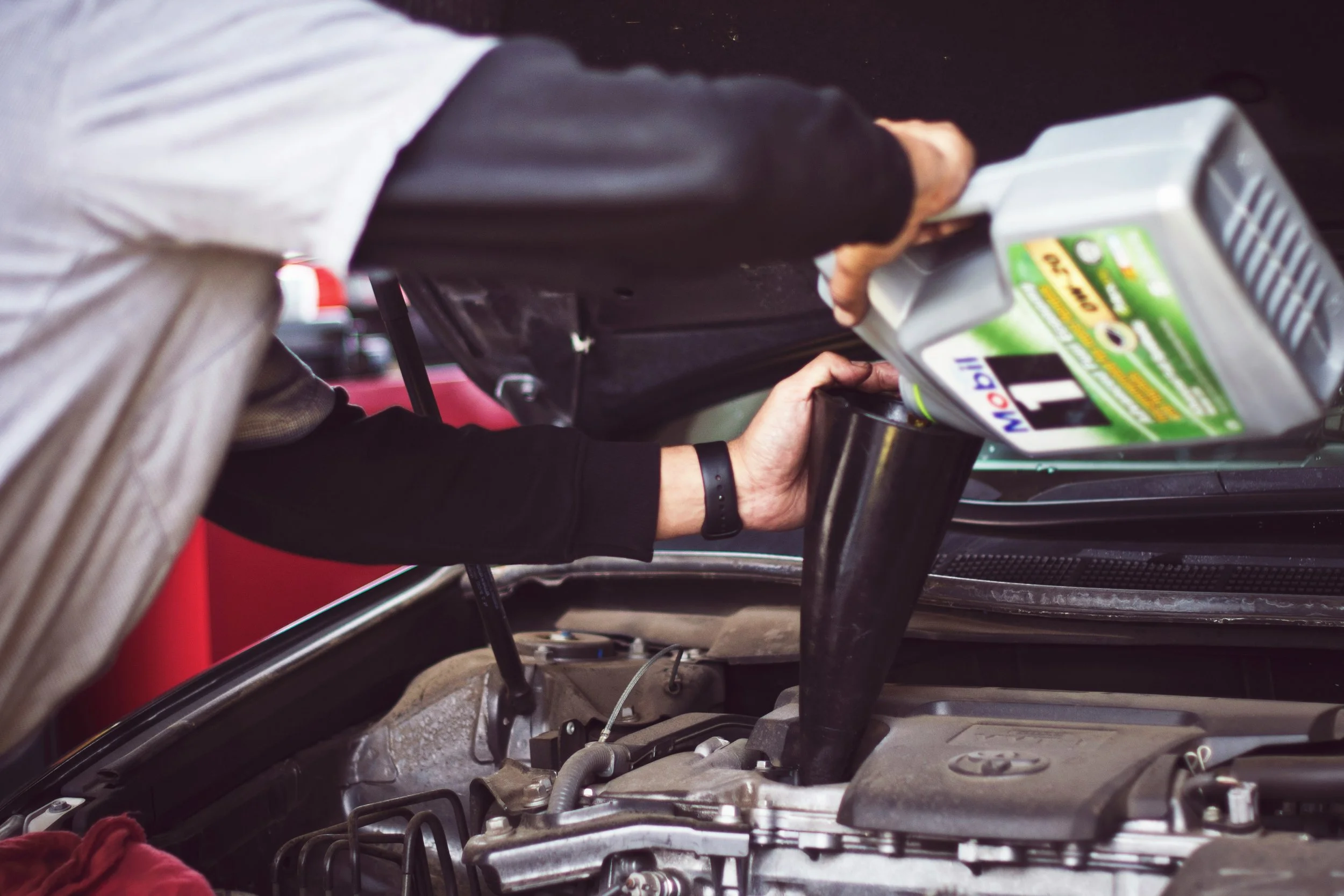 Person pouring motor oil from a container into a car engine.