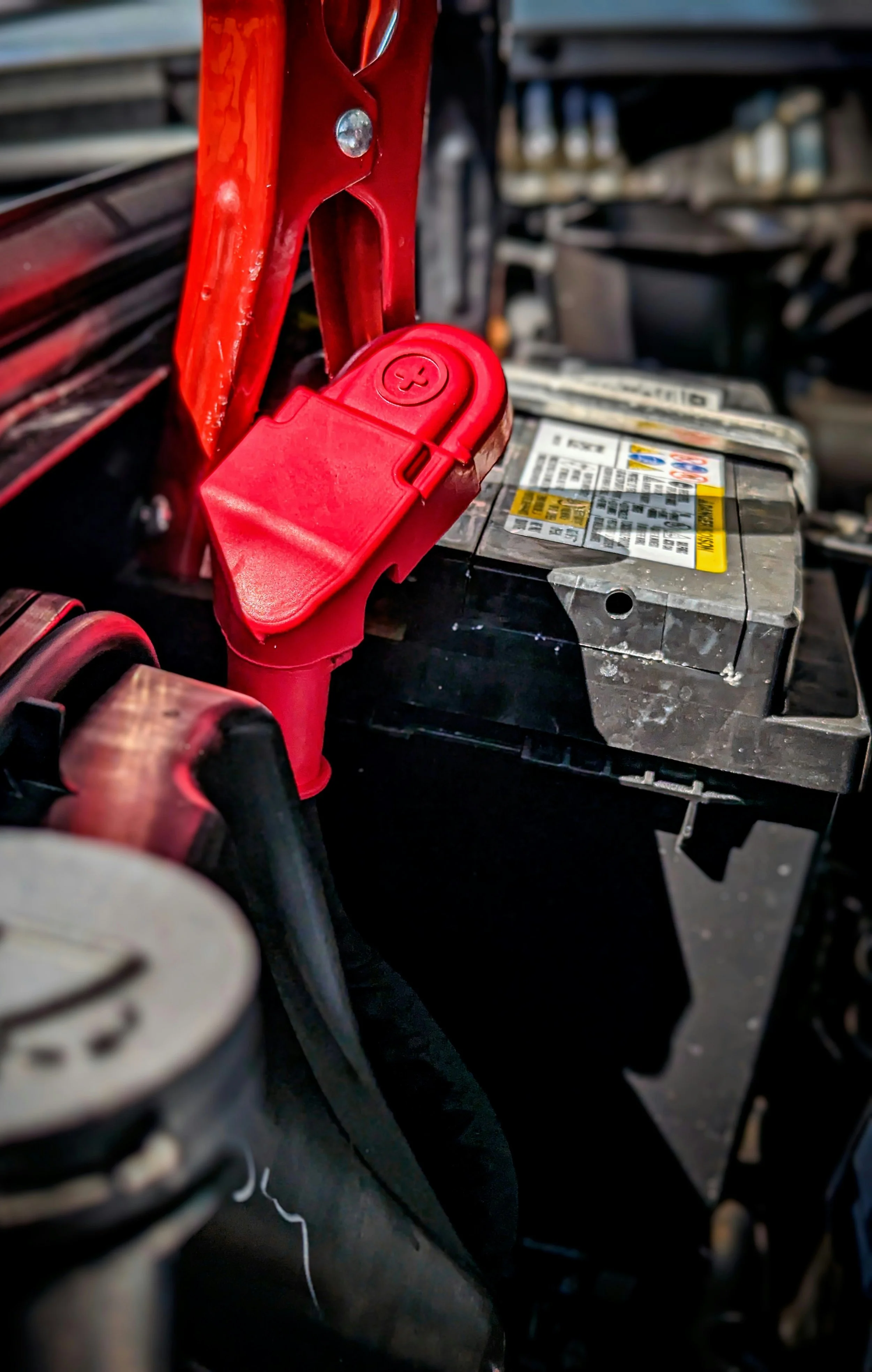 Close-up of a car battery with a red terminal cover and cables inside a vehicle engine compartment.
