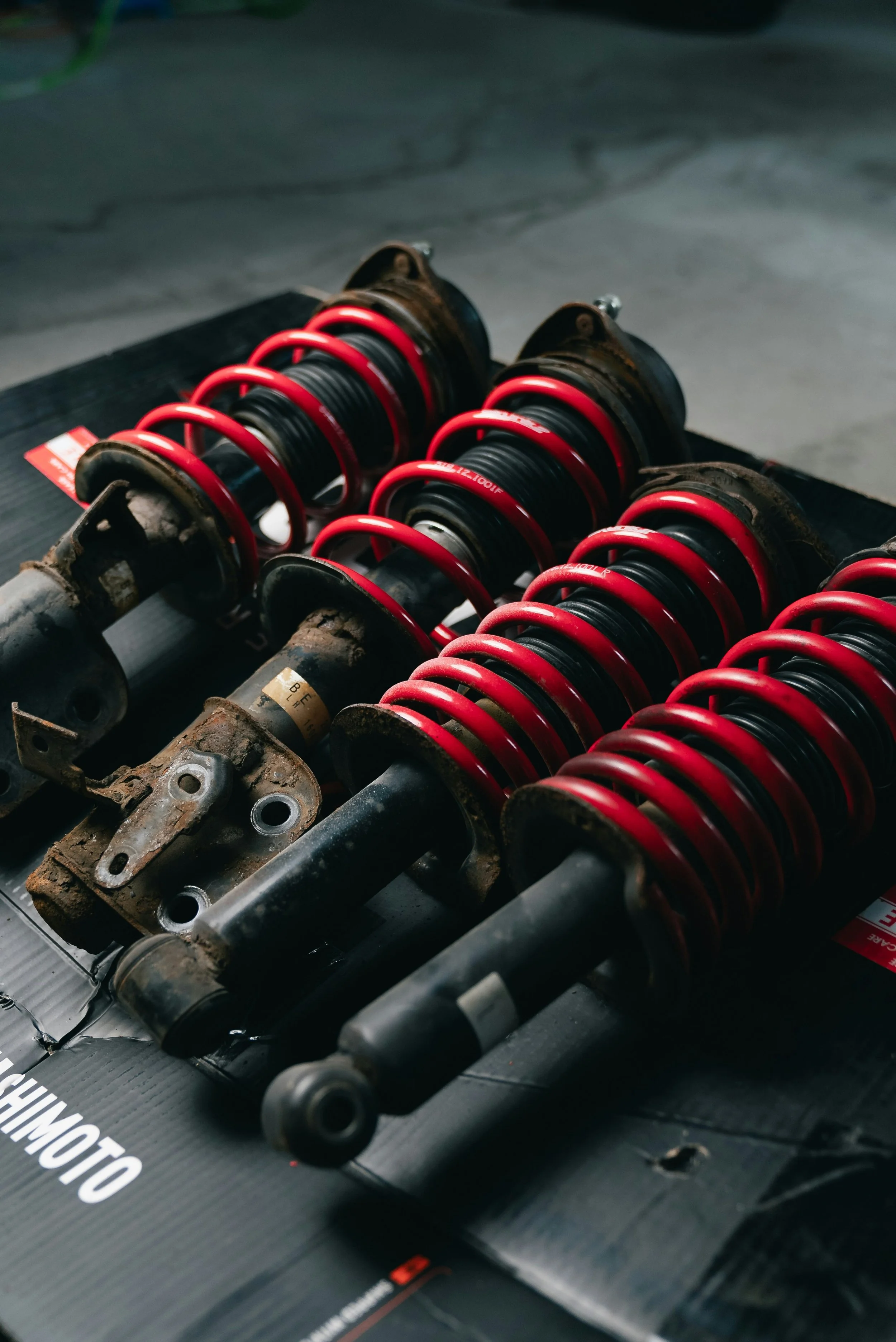 Close-up of a set of old, used car shock absorbers with red springs, resting on a black surface.
