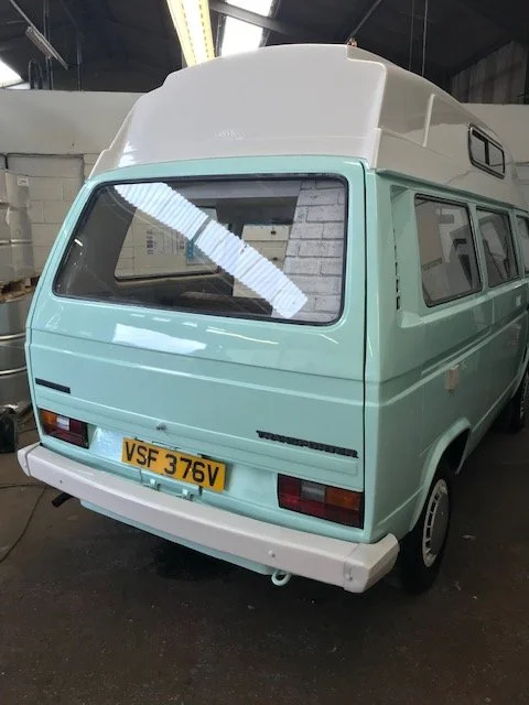 A vintage light blue camper van with a white roof parked inside a warehouse.
