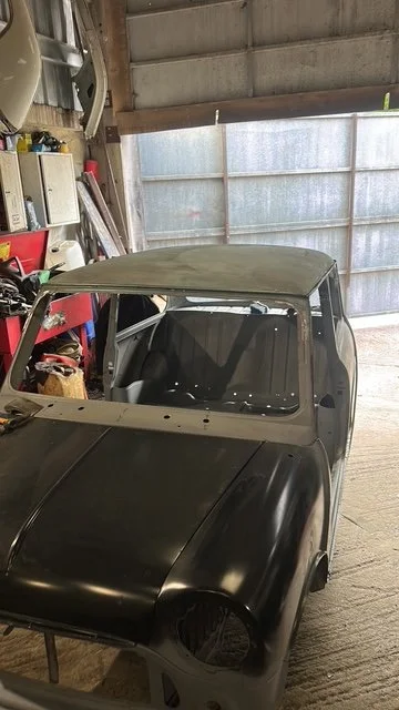 Partially assembled vintage car inside a garage, with a black hood and a stripped roof.