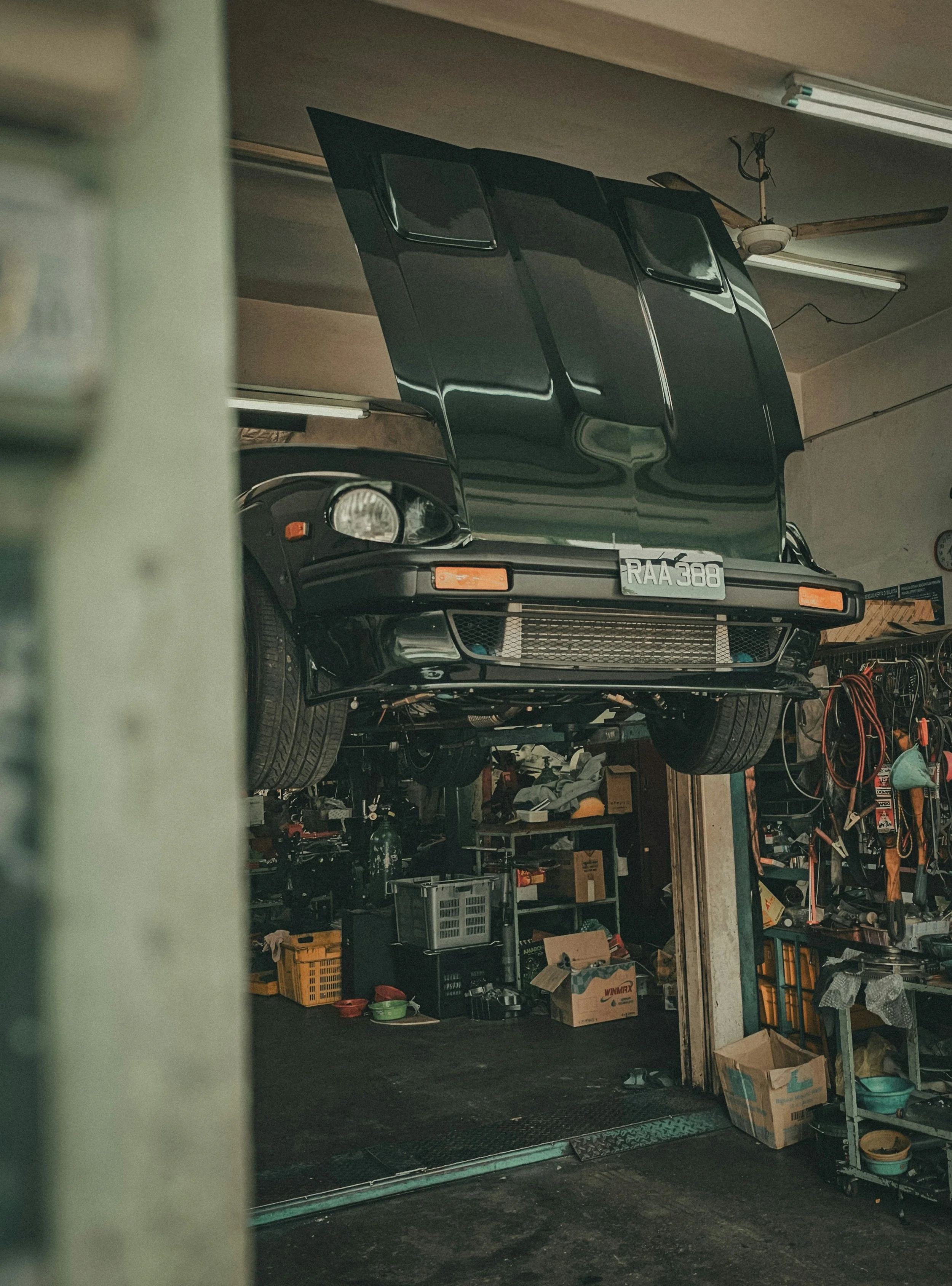 Garage with a black sports car elevated on a lift, surrounded by tools, storage bins, and boxes.