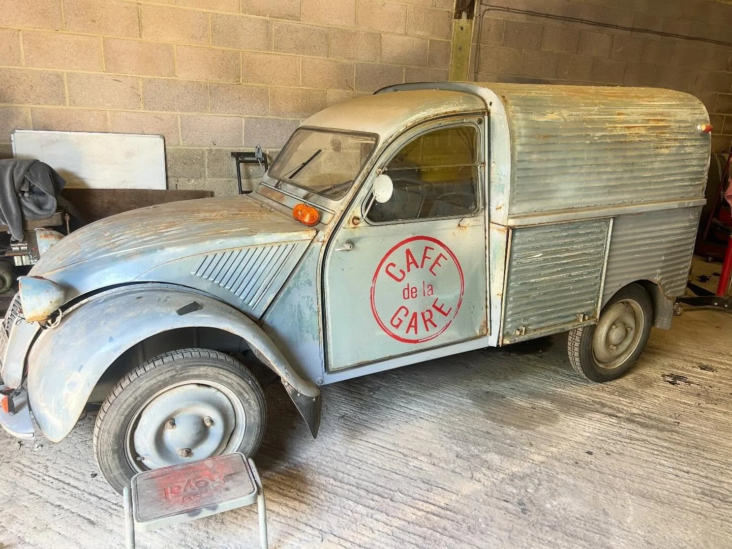 Vintage Citroën Méhari with a rustic, weathered look and signage reading 'CAFÉ de la GARE' on the door, parked indoors on a concrete floor.