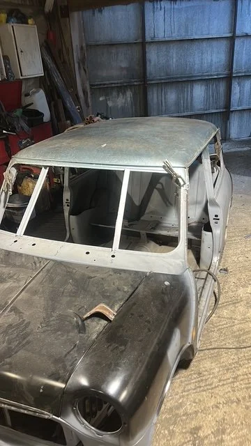 Old, dusty, weathered car inside a garage, with parts missing and signs of age.