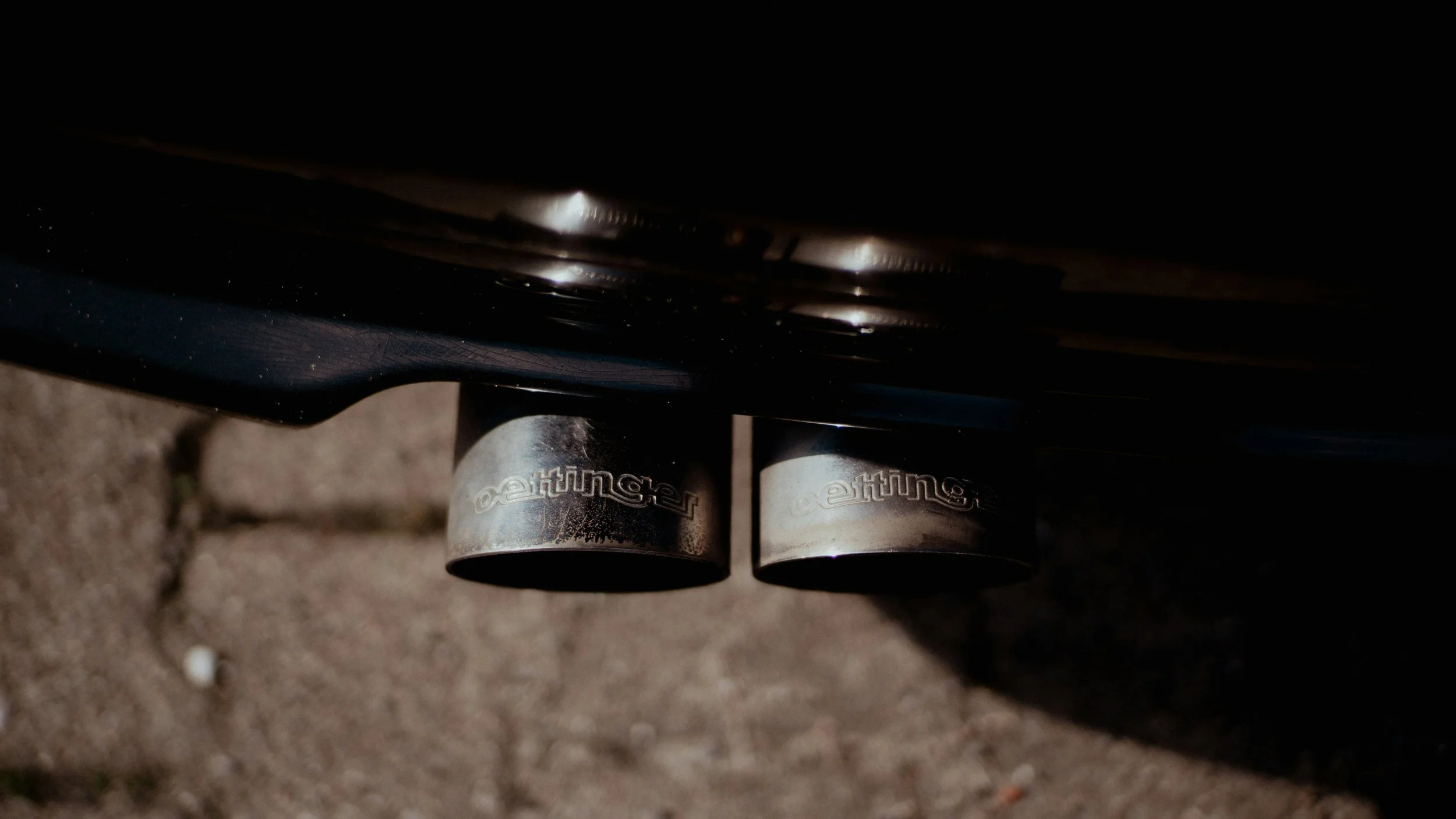 Close-up of two car exhaust pipes beneath a black car with blurred background.