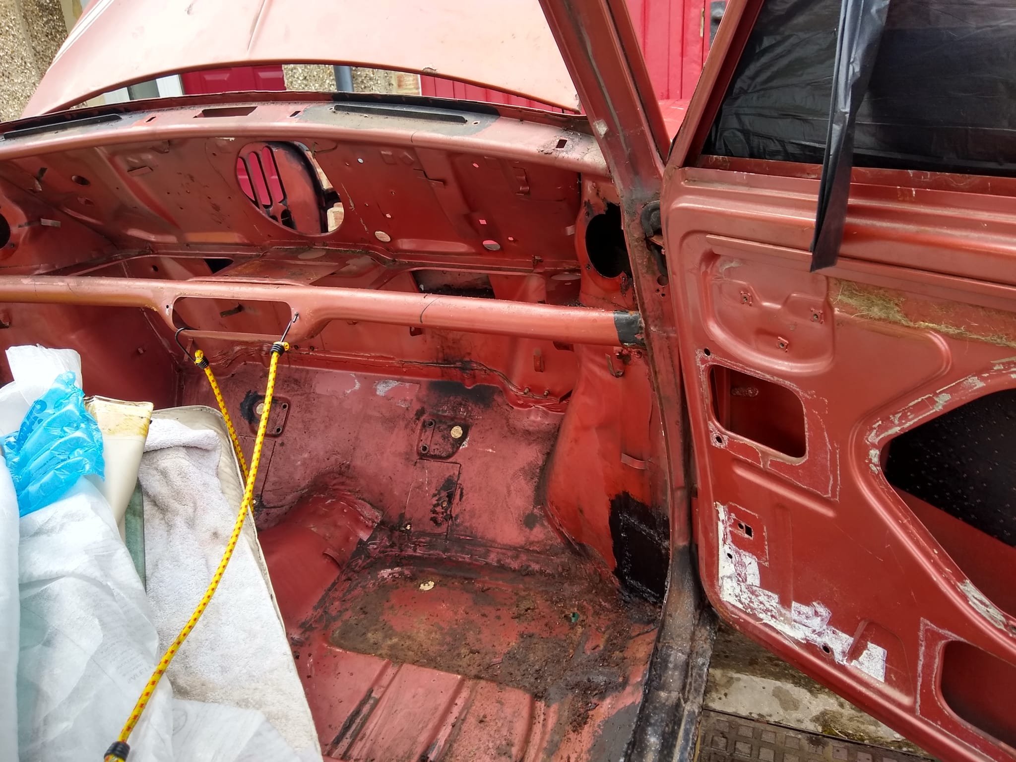 Empty red vehicle interior with no seats, exposed metal, and some debris and dirt on the floor and walls.