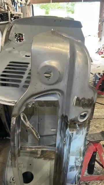 Close-up of a metal car body panel in a workshop with a red jack stand in the background.