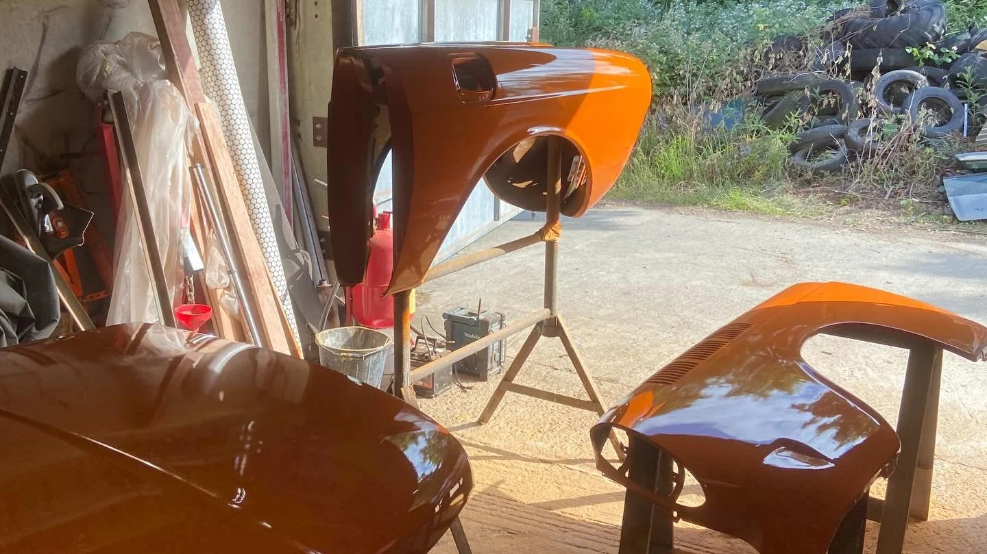 Car parts painted in orange on stands inside a garage, with tires and miscellaneous items in the background.