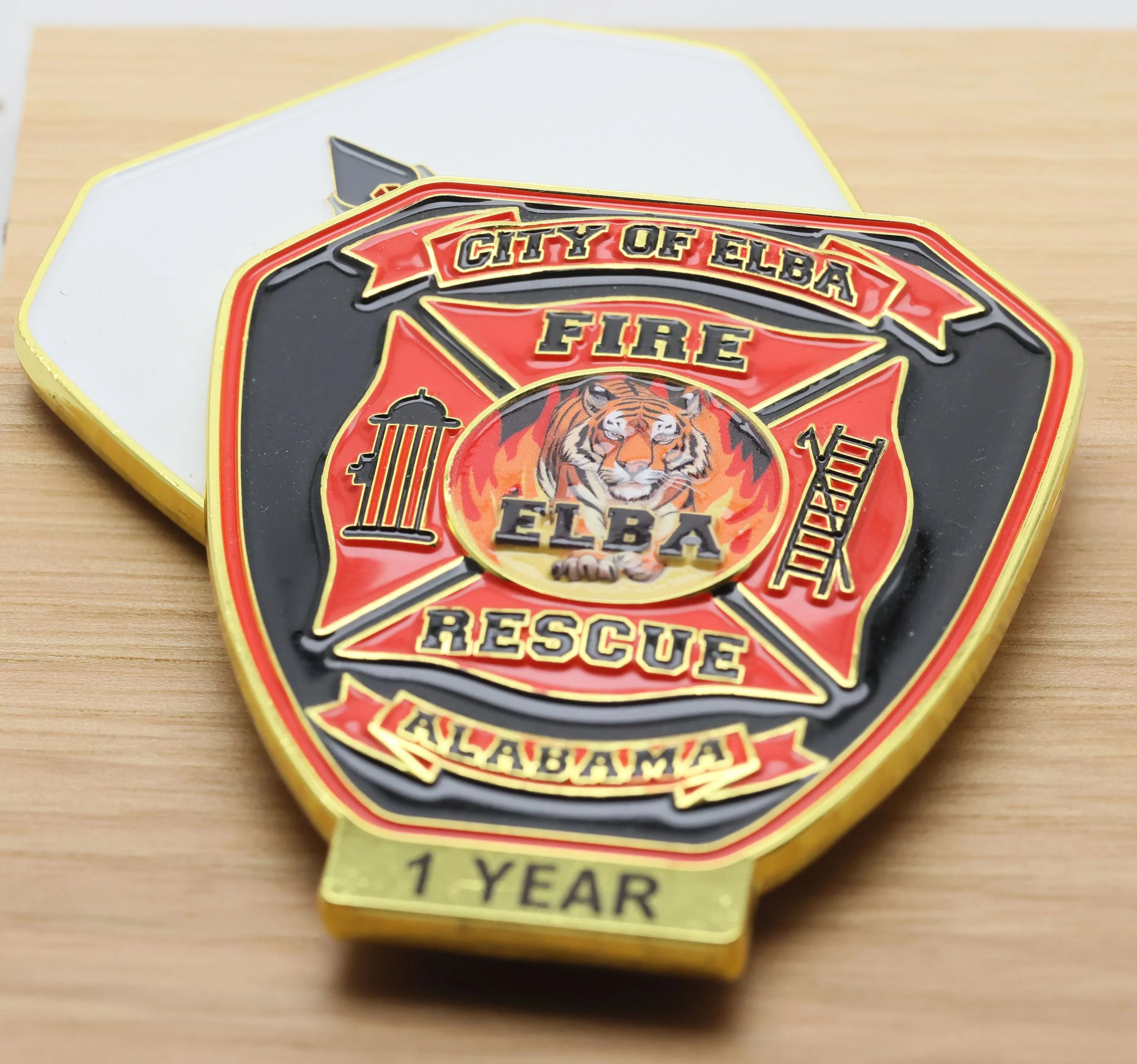 Close-up of a challenge coin with a tiger illustration and the text 'City of Elba Fire Rescue', celebrating 10 years.