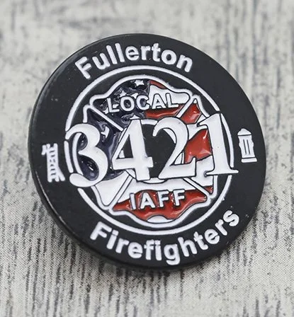 Fullerton Firefighters Local 3412 pin with the number 3421, featuring a fire truck, a firefighter axe, and a fire hose, on a wooden surface.
