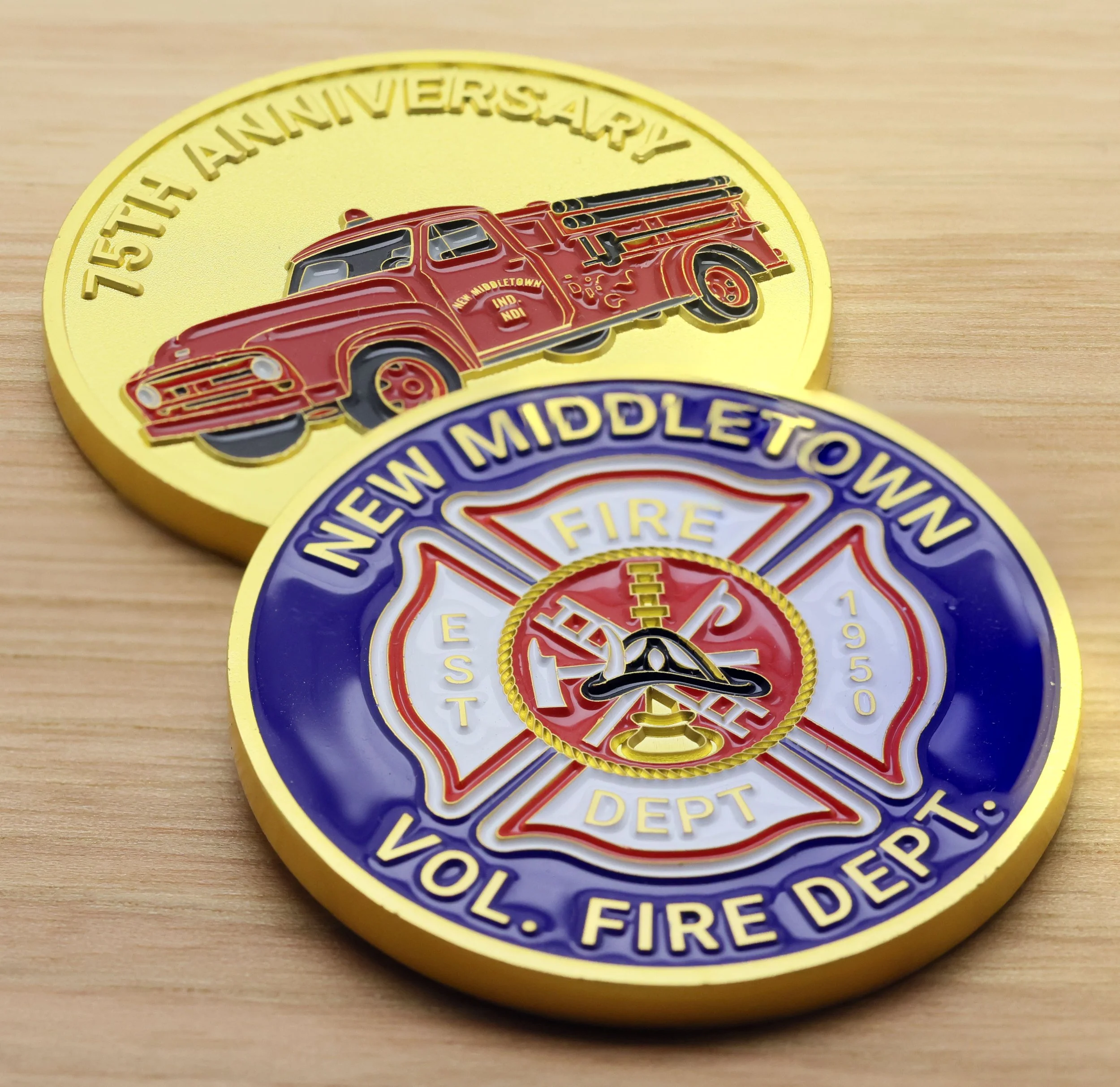 Close-up of a challenge coin for the 75th anniversary of the New Middletown Fire Department, featuring a red fire truck and gold and purple lettering.