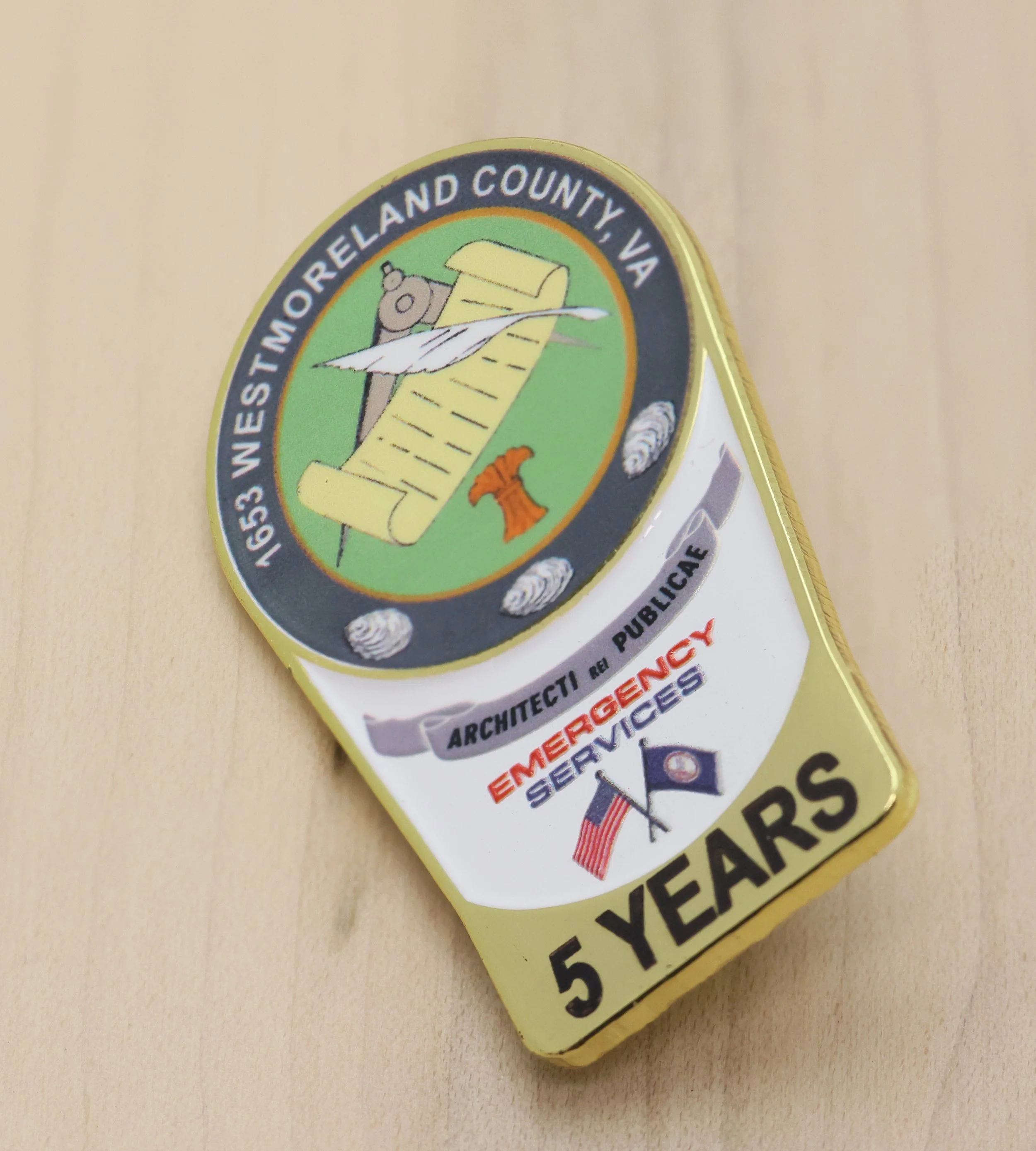 Close-up of a years of service pin with the text 'Wests Moreland County, VA' and a cartoon bear holding a scroll and a brass horn.