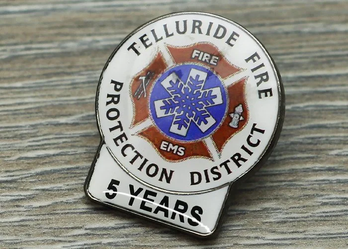 A years of service pin for Telluride Fire Protection District, celebrating 5 years, featuring a snowflake symbol with fire and EMS symbols inside, on a wooden surface.
