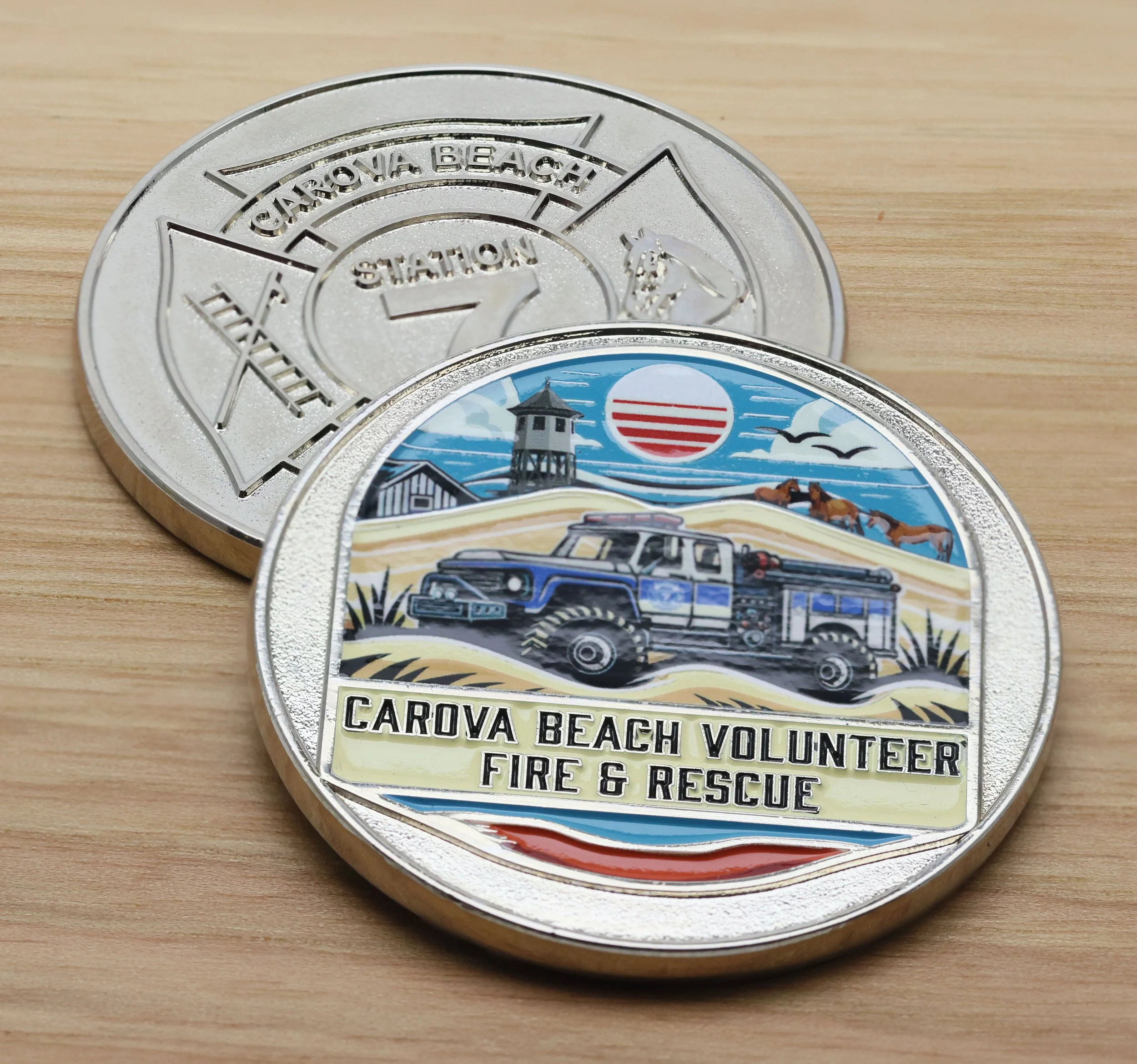 Close-up of a silver challenge coin with a scenic image of a lighthouse, seagulls, and water, with the words 'Carova Beach Volunteer Fire & Rescue' at the bottom.