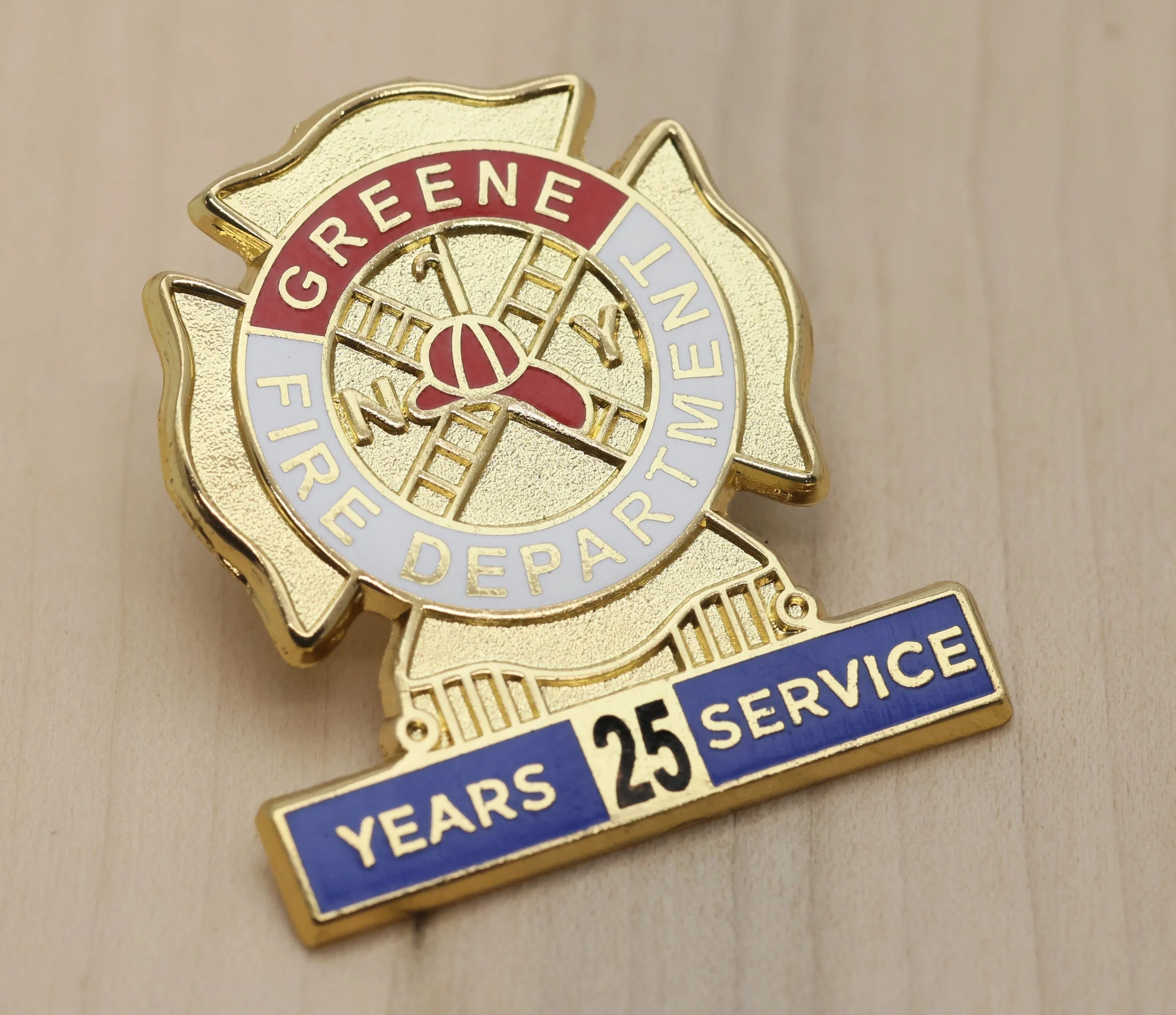 Close-up of a gold-colored firefighter years of service pin with red, white, and blue accents, displaying the text 'Greene Fire Department' and indicating 25 years of service.