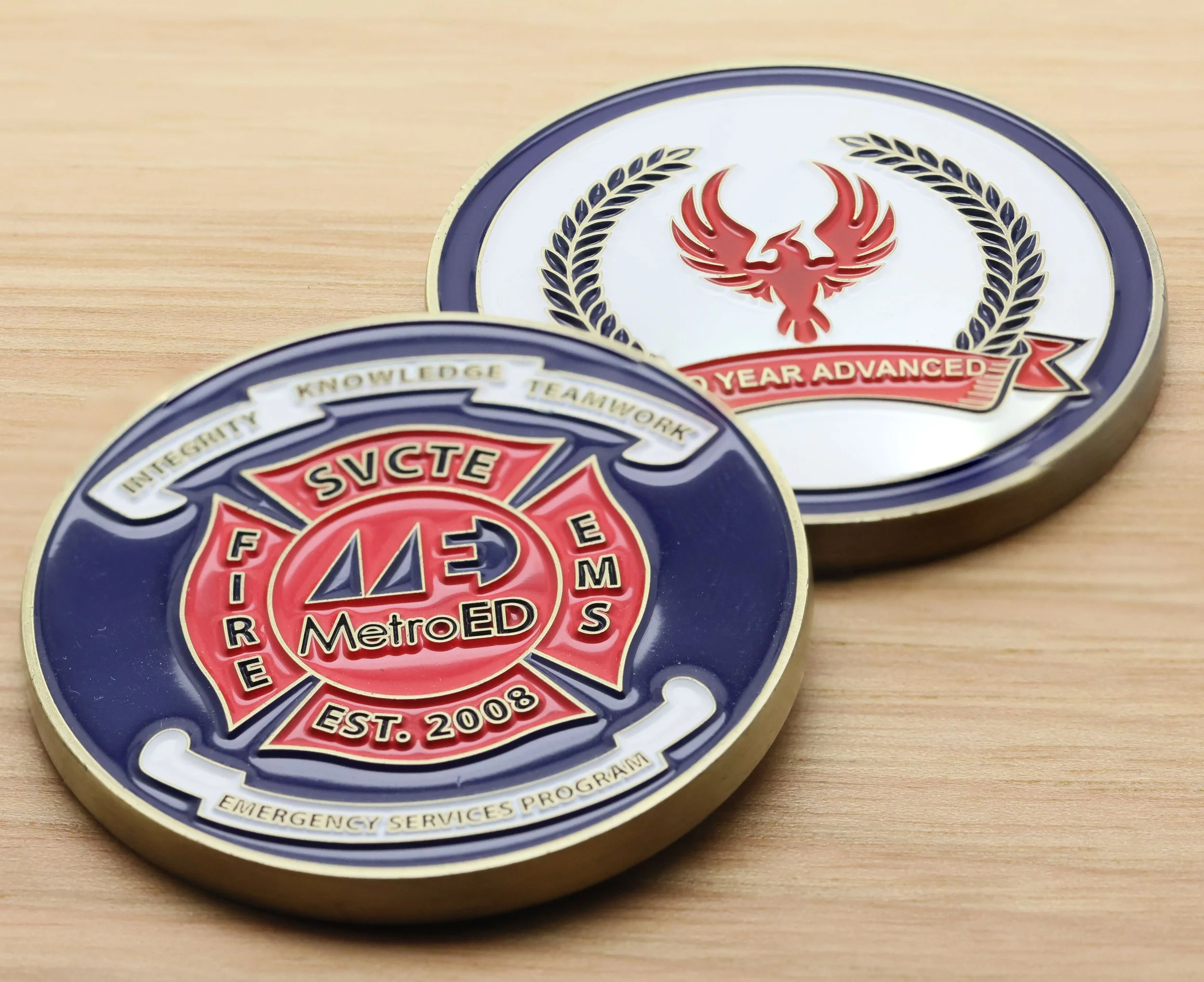 Close-up of challenge coins with a red phoenix emblem in the center, badge features blue, white, red, and gold colors, and text indicating 20 years of service for Metro EMS, established in 2008.