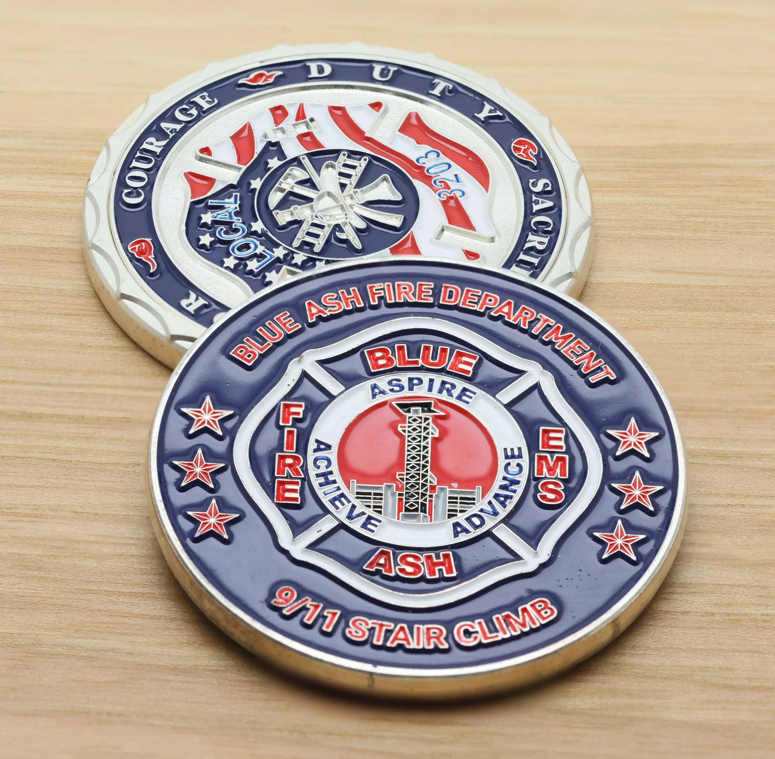 Close-up of a challenge coin with the words 'Blue Stair Climb' and the phrase 'in the Blue Ash Fire Department' surrounding a fire department tower ladder, with red, white, and blue design elements, resting on a wooden surface.