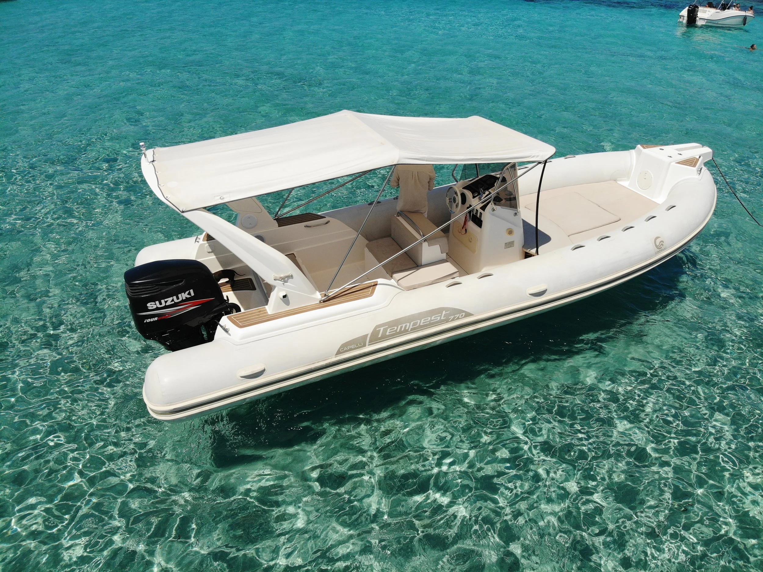 A white motorboat with a shaded canopy floating on clear turquoise water with other boats in the background.