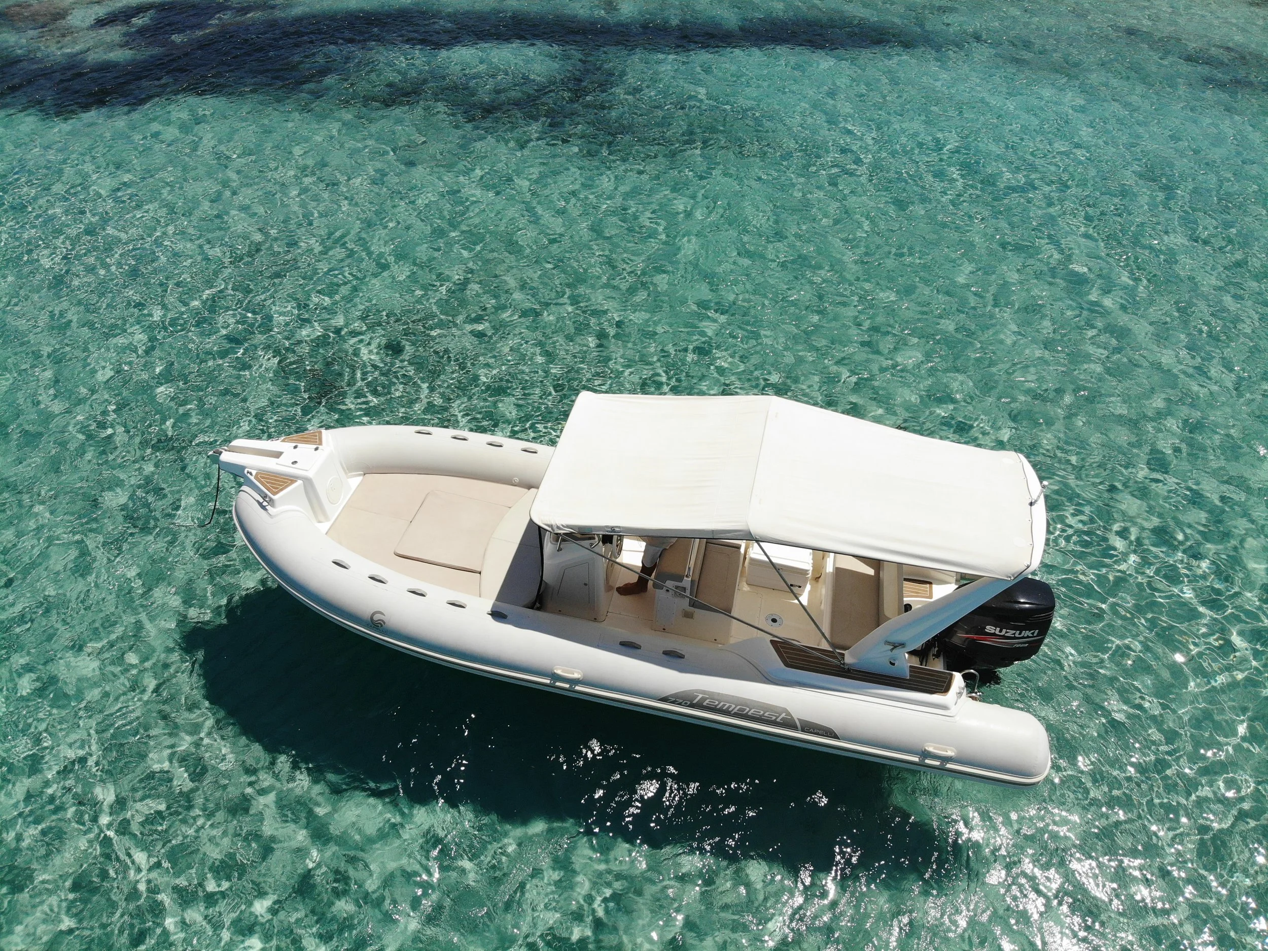A white motorized boat floats in clear turquoise water, with a white sunshade on top and a Suzuki outboard motor at the back.