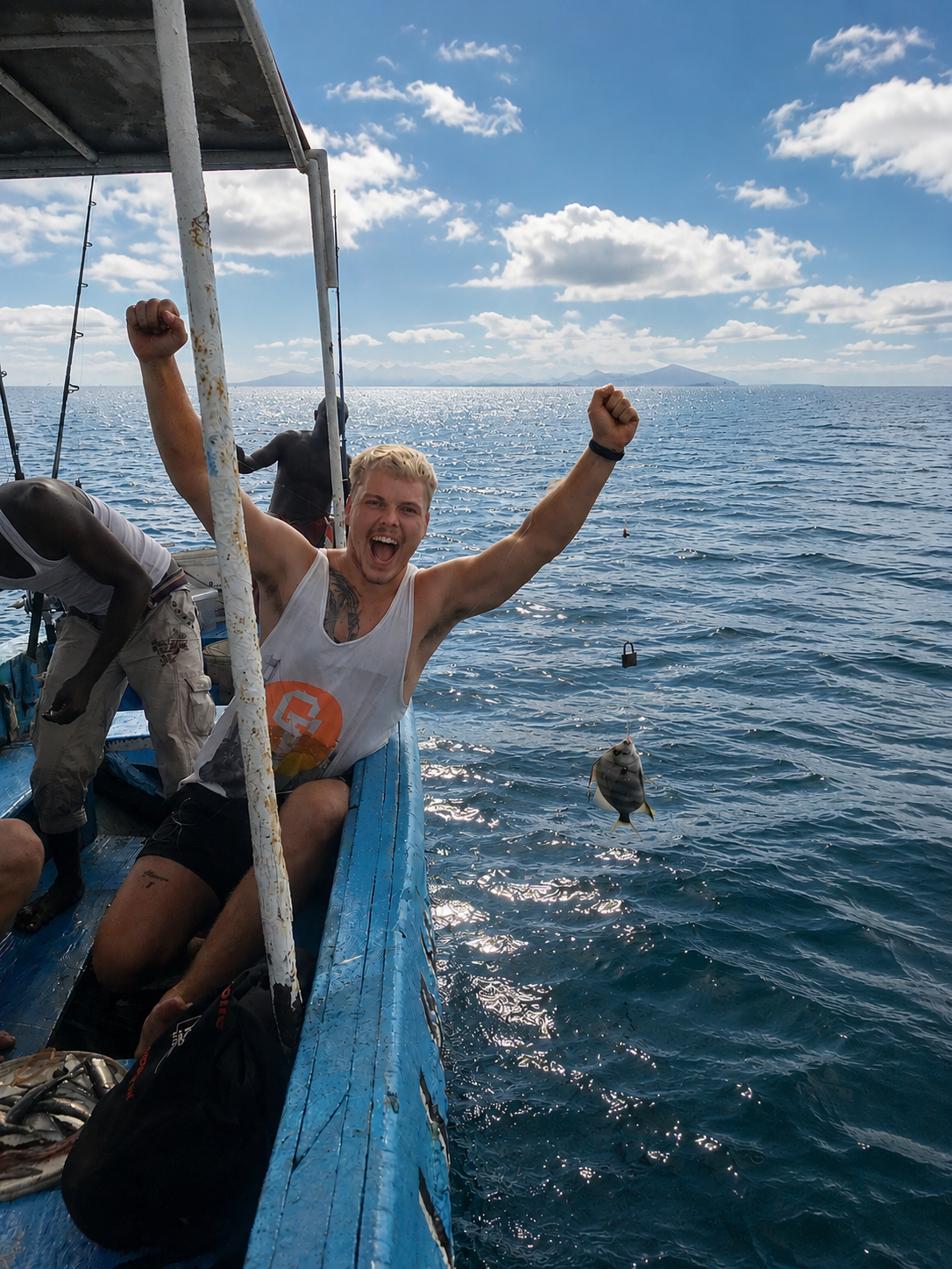 A man on a boat celebrating with raised fists after fishing a fish out of the water, with a clear blue sky and ocean in the background.