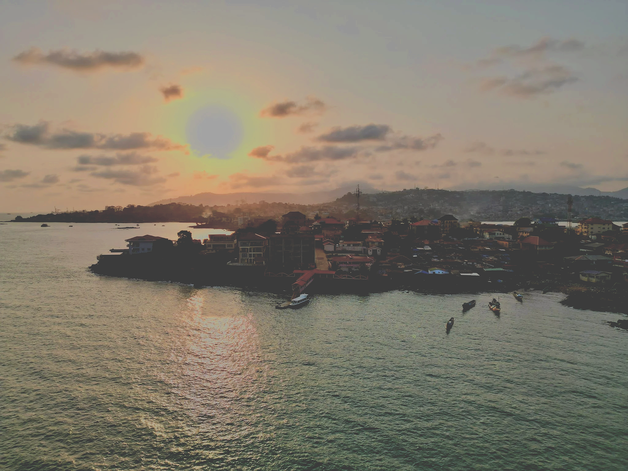 Solnedgang over Freetown med hav, både og byens grønne bjerge i baggrunden.
