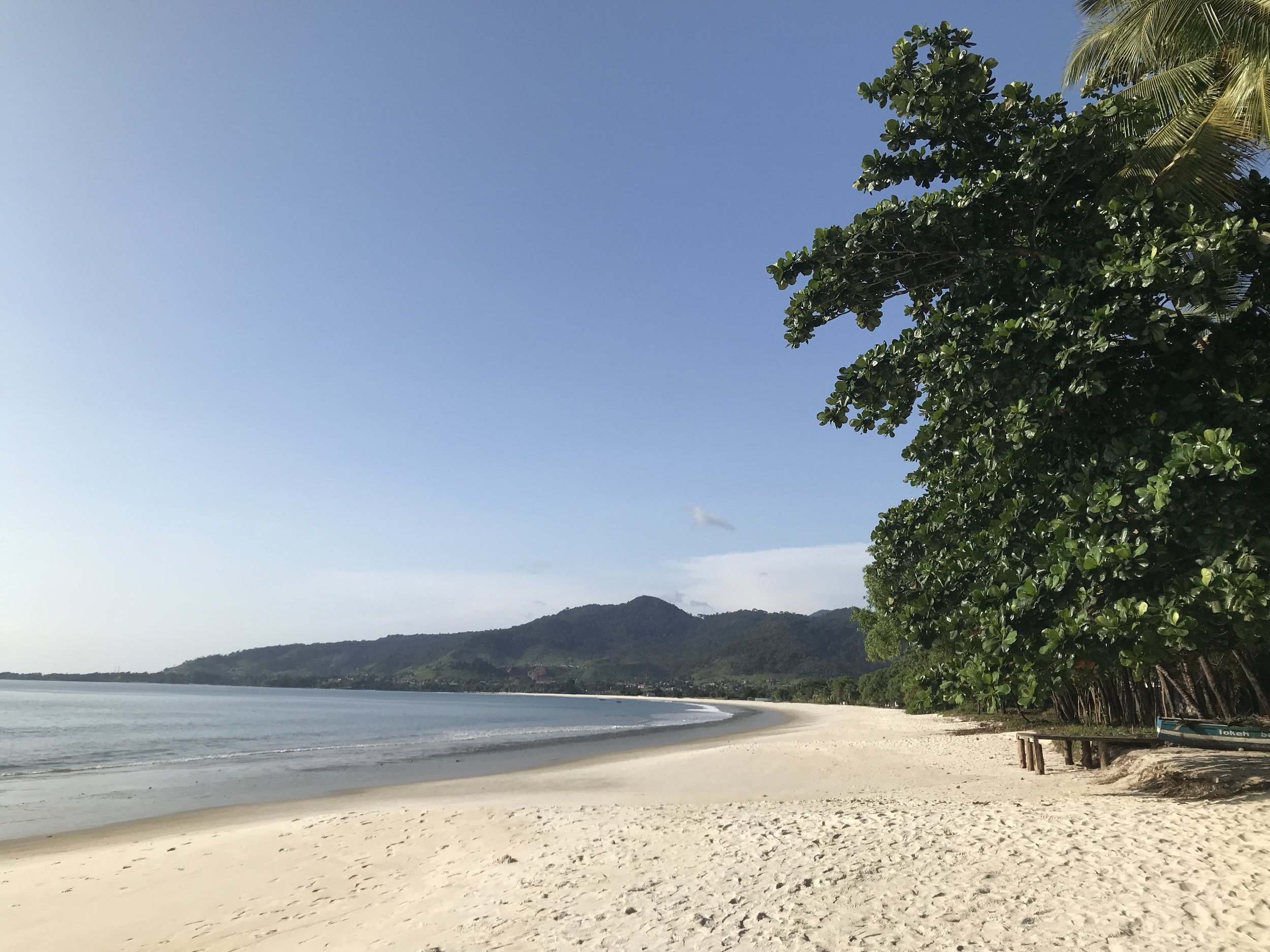 Tokeh Beach i Sierra Leone med hvid sandstrand, roligt hav og grønne bjerge i baggrunden.