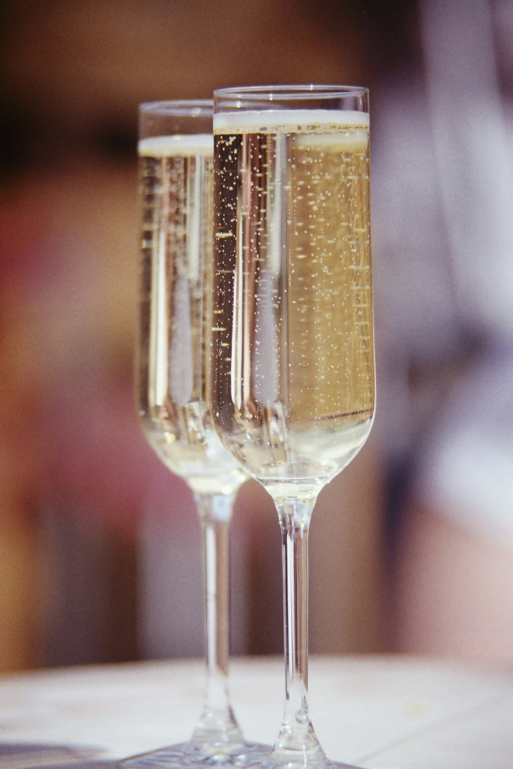 Two tall flutes of champagne with bubbles, arranged on a table with a blurred background.