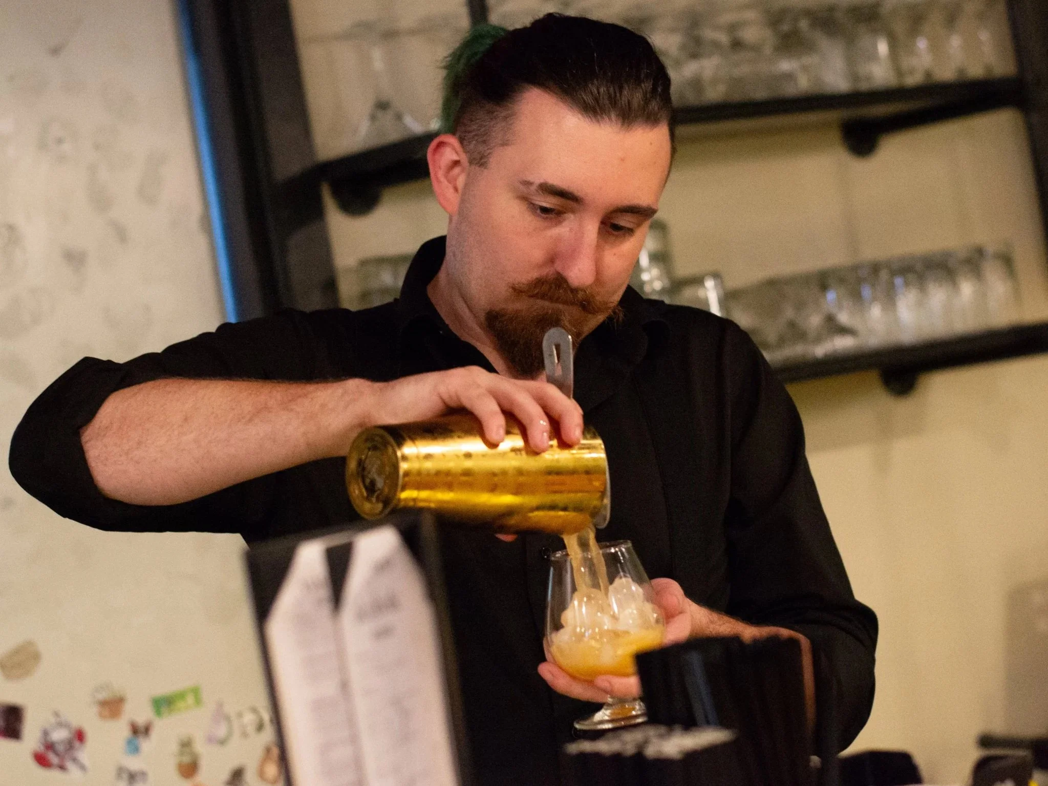Man with dark hair and beard pouring beer into a glass at a bar or restaurant.