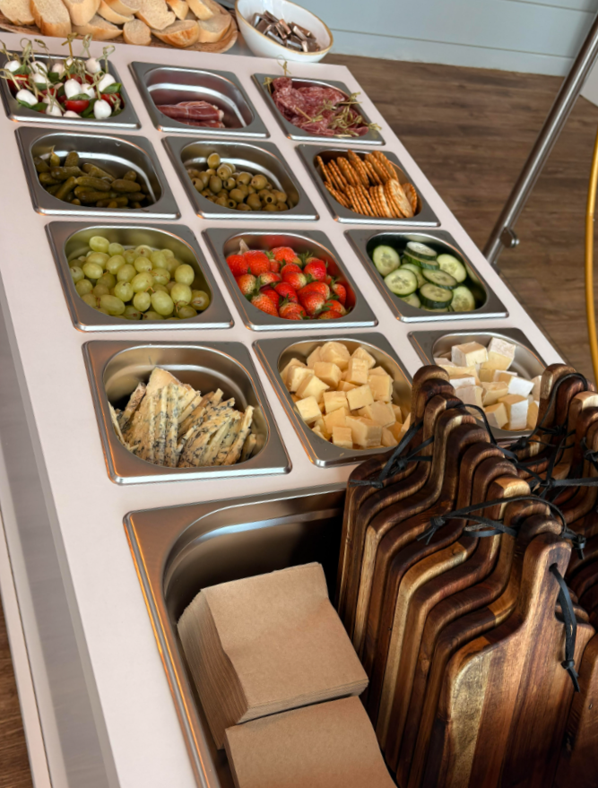 A salad bar with various fresh vegetables, cheeses, meats, and crackers, along with paper napkins at the front.
