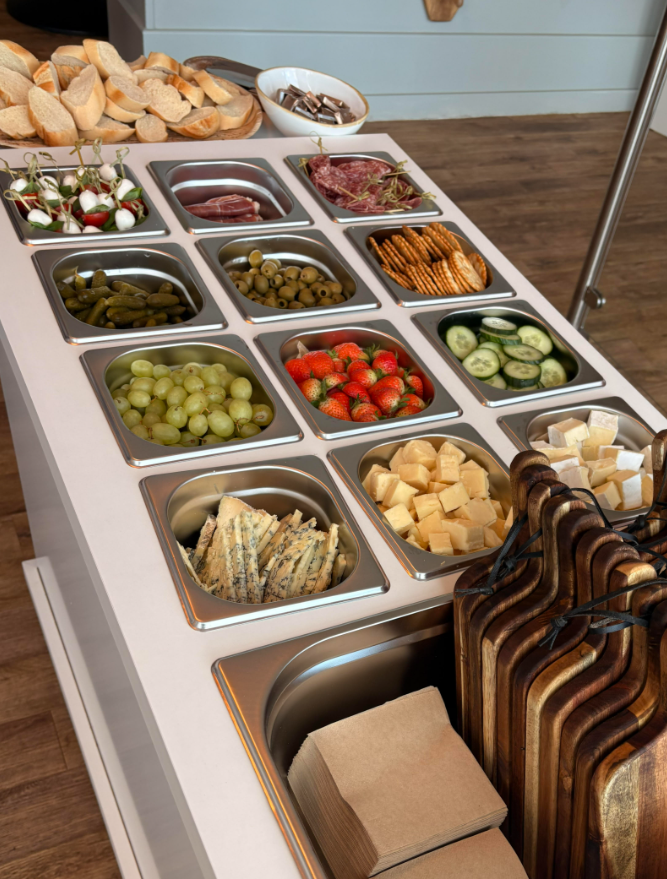 A buffet table with various foods including bread, grapes, strawberries, cucumbers, cheese, greens, and sliced meats.
