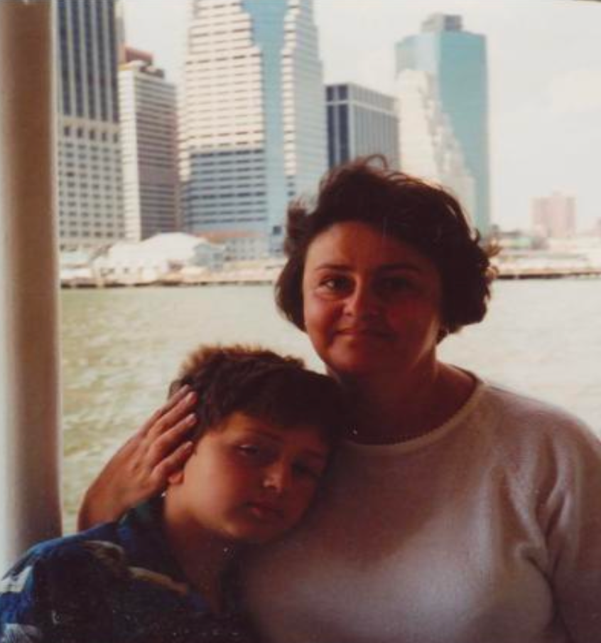 A woman and a boy posing together near a body of water with a city skyline in the background.