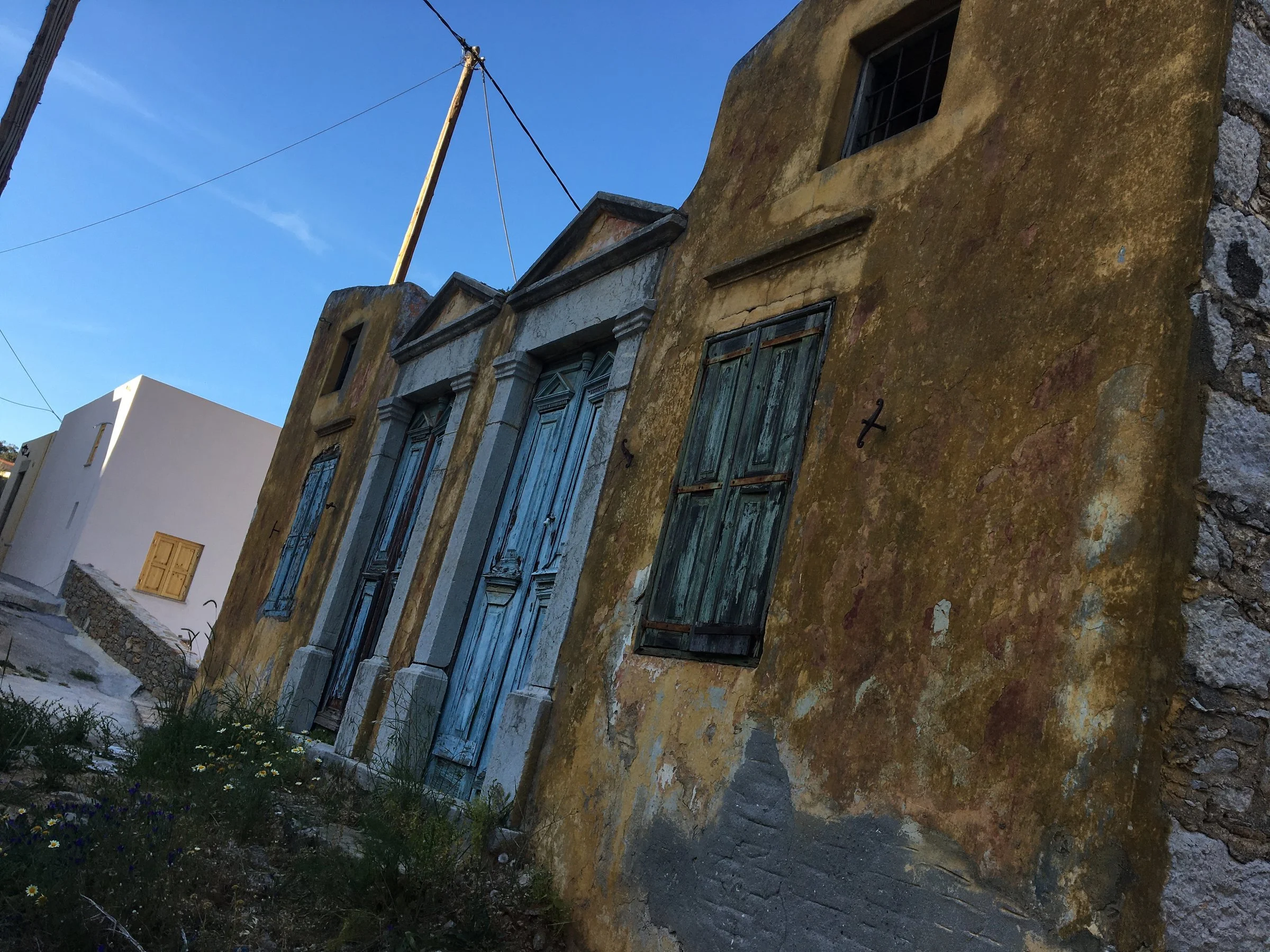 The striking silhouette of an abandoned, decaying building standing proudly against a clear blue Aegean sky.