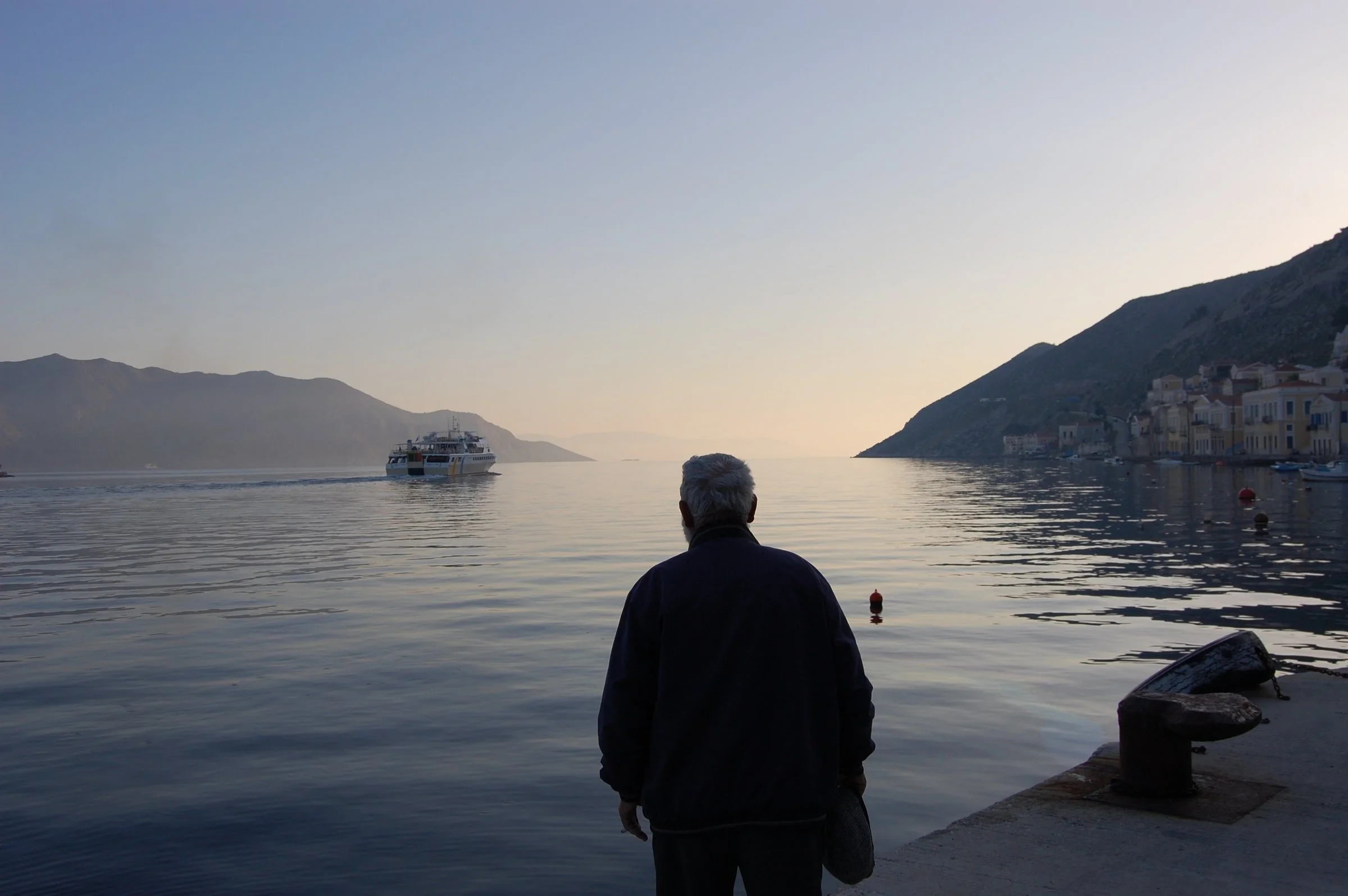 A fine art photograph titled 'Ones Left Behind', capturing a solitary silhouette against the misty, atmospheric horizon of the Aegean sea.