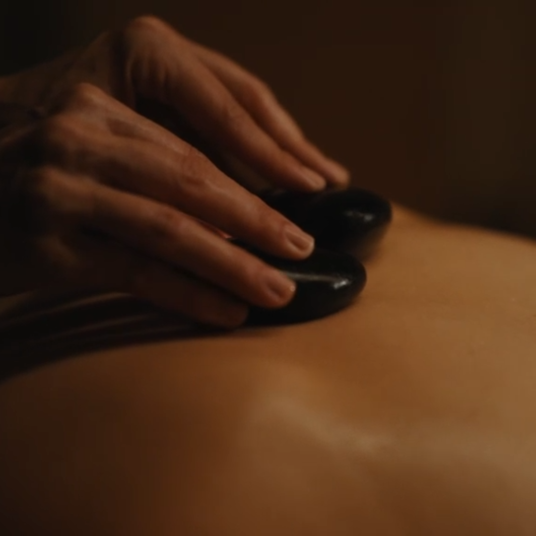 Close-up of a hand massaging a person's back with hot stones in a spa or massage setting.