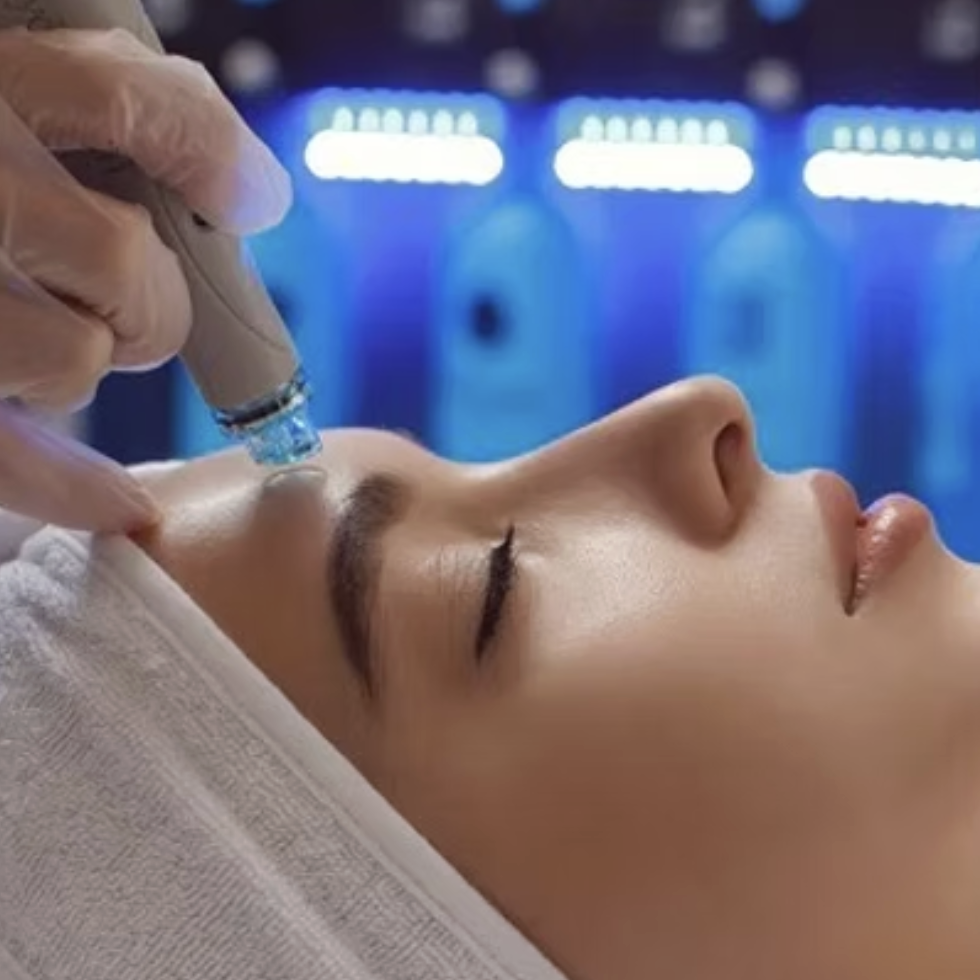 A woman receiving a facial treatment with a clear liquid being applied to her forehead in a clinical setting.