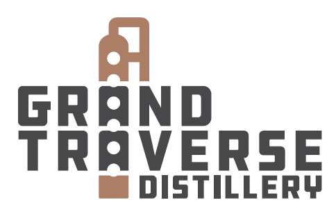 White background Text in black saying Grand Traverse Distillery with a brown image that implies a distiller