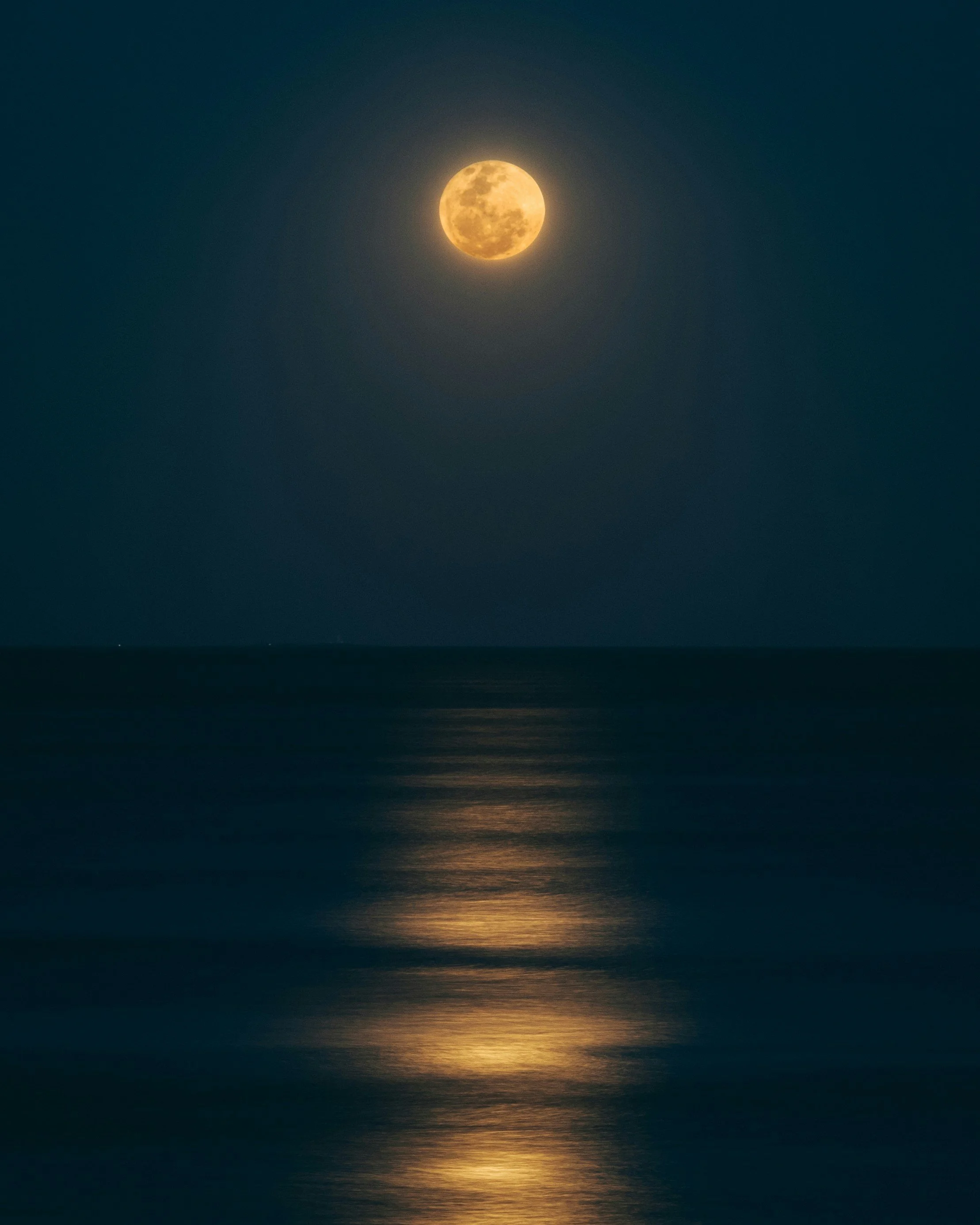 Photo of the Moon reflecting yellow light in the night sky casting light onto the lake below