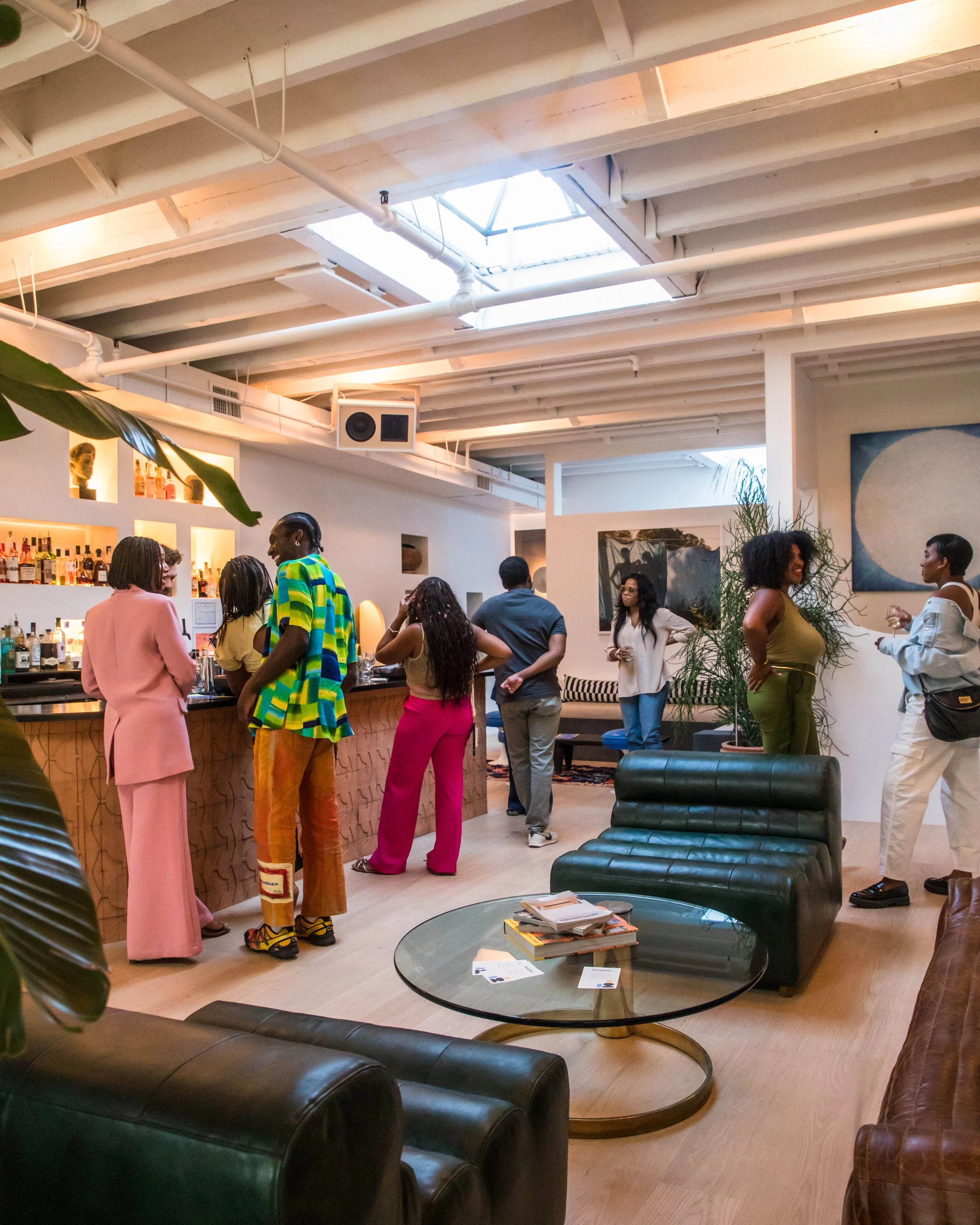People socializing in a modern, well-lit living room with a bar, artwork, and large windows.