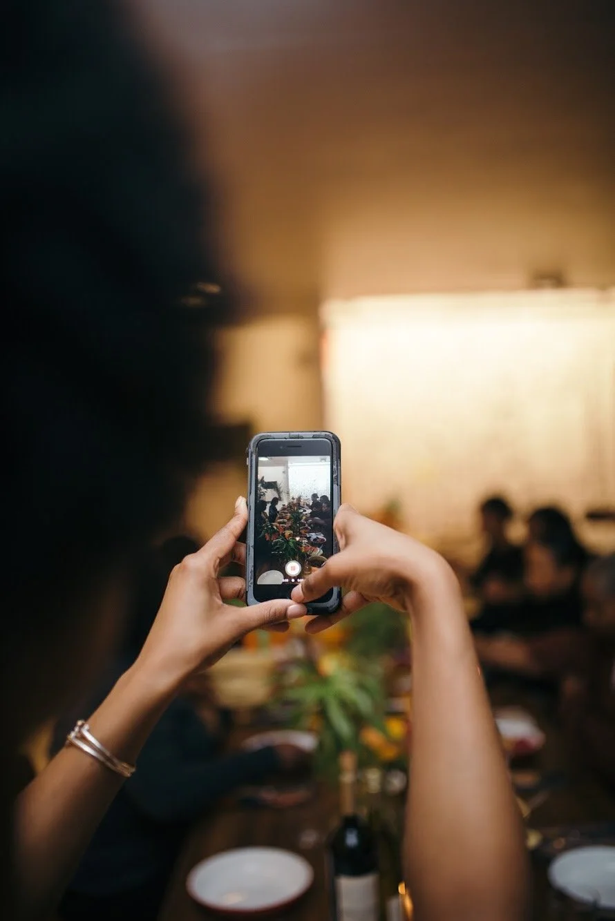 Shanika Hillocks taking a photo of a dining scene with a smartphone at a restaurant.