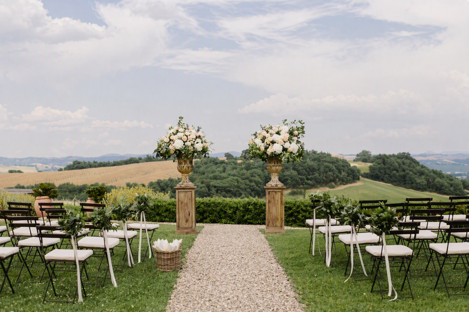 Elegant outdoor wedding setup with an aisle, floral arrangements, and a scenic countryside view.