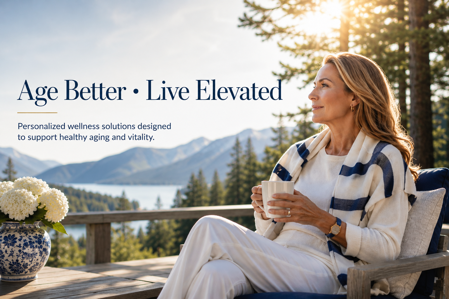 A woman sitting outdoors on a wooden deck, holding a white mug, with mountains, trees, and a lake in the background, sun shining through the trees.