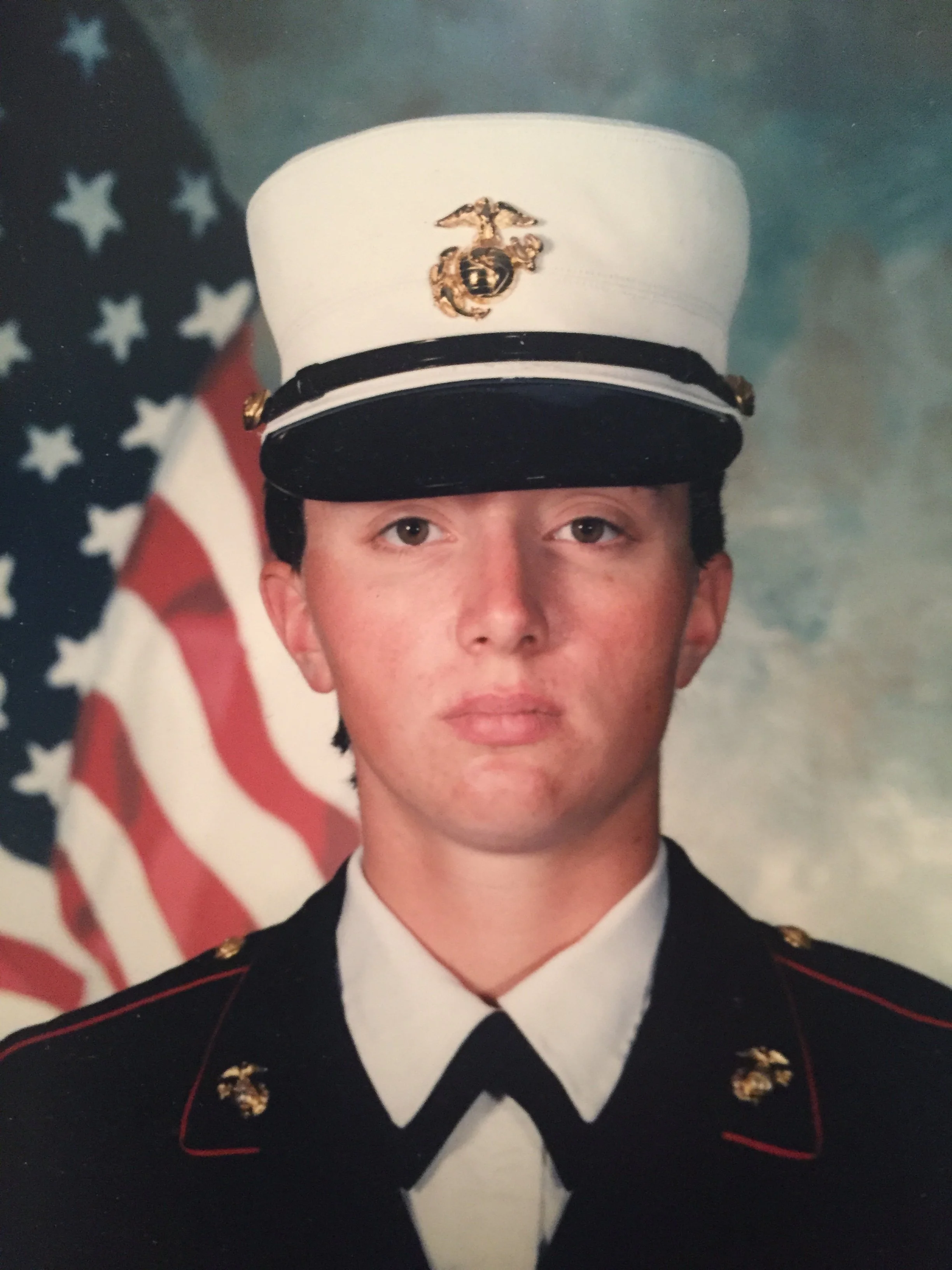 Young man in United States Marine Corps dress uniform standing in front of an American flag