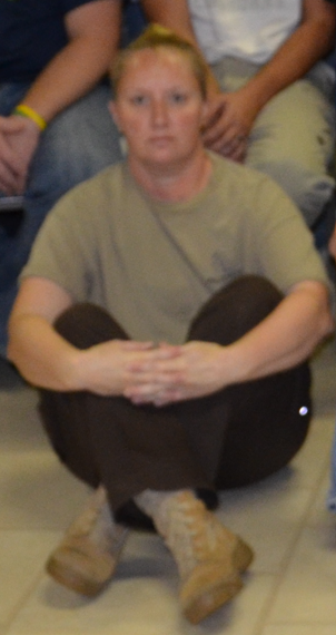 Person with short blonde hair sitting cross-legged on the floor in casual clothing.