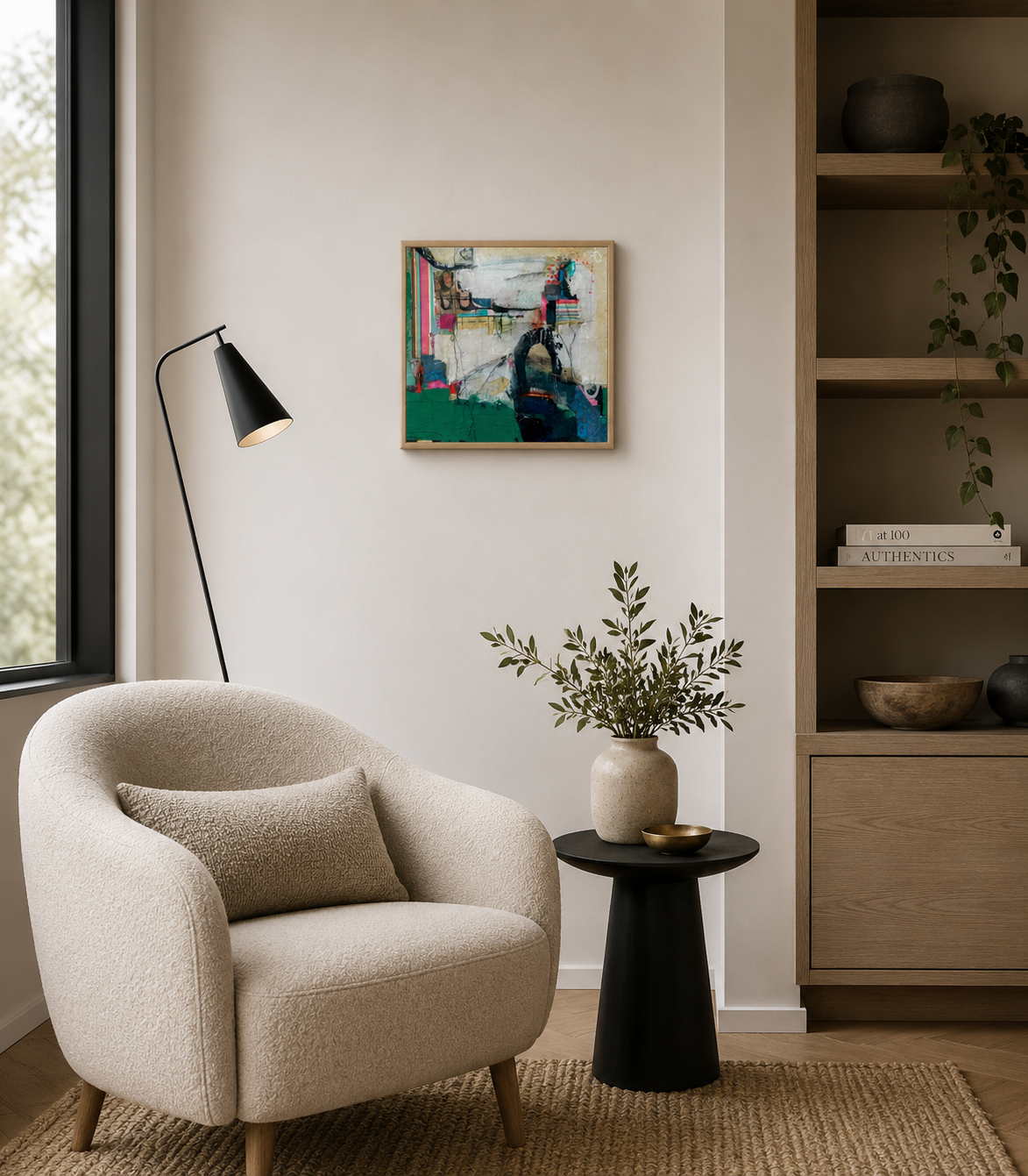 Cozy living room corner with beige armchair, a black side table with a vase and green foliage, a black floor lamp, a wall art painting, wooden bookshelf with decorative items and books, and a window with natural light.