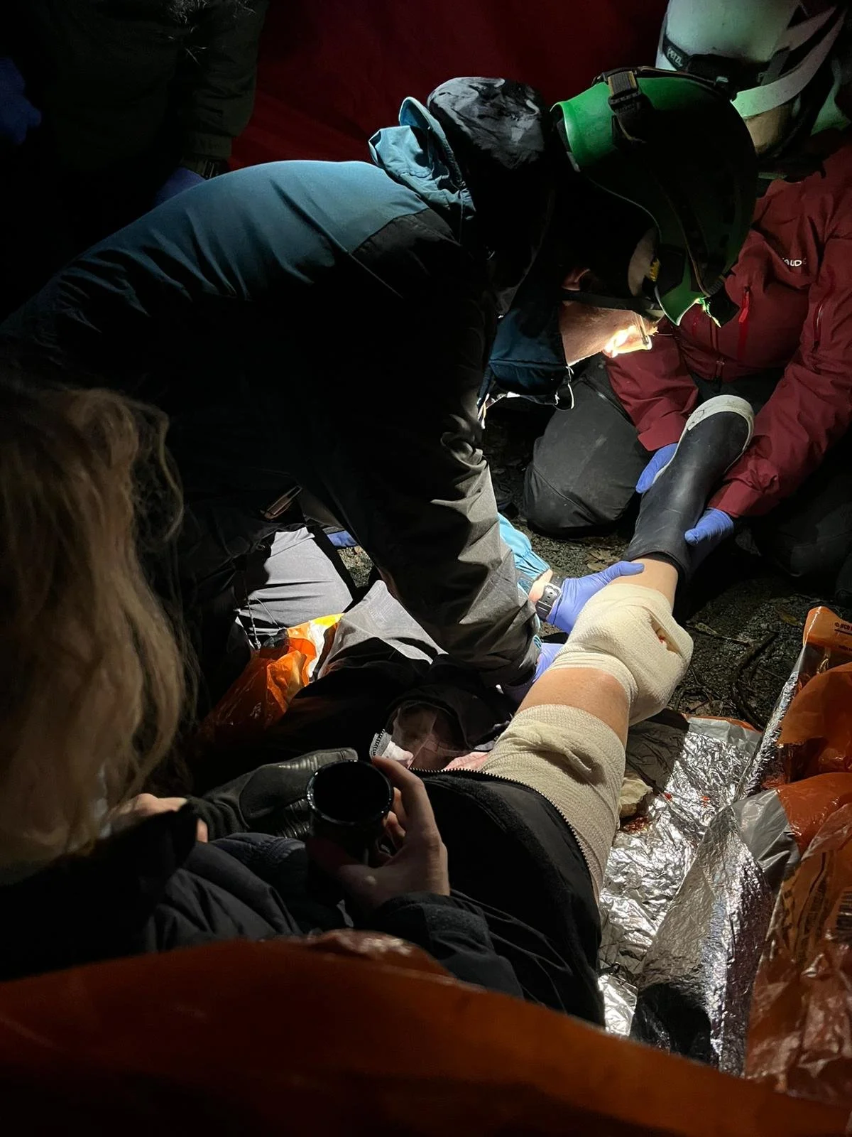 Rescue team tending to an injured person lying on the ground, with medical supplies and gear around them.