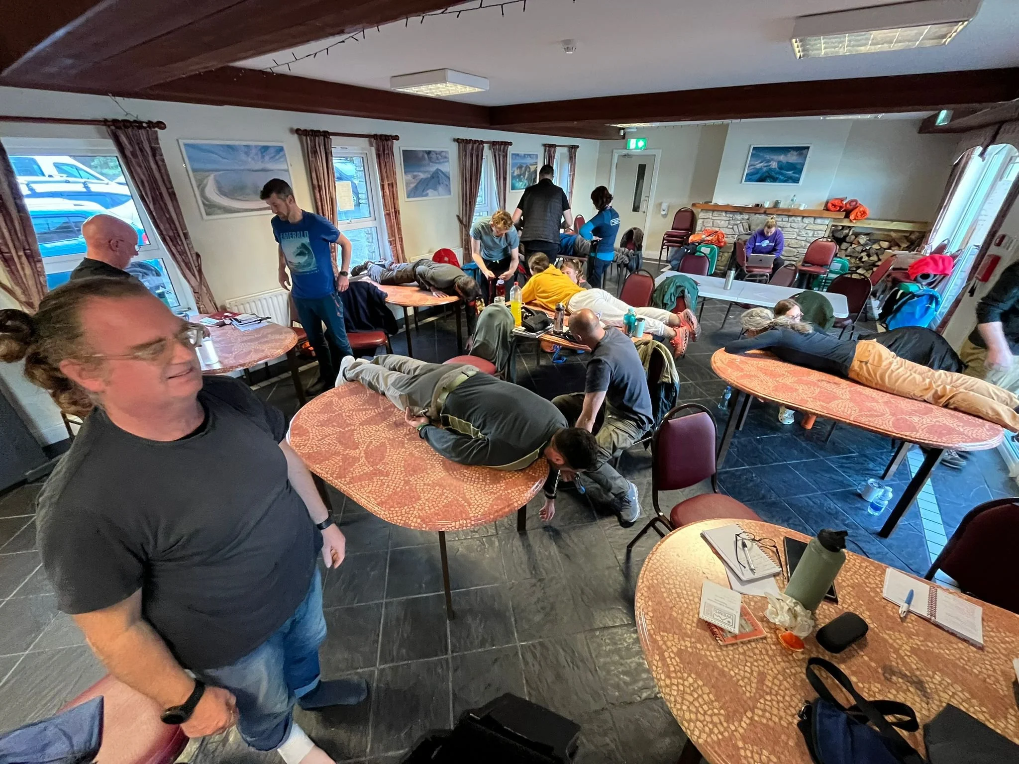 People practicing first aid on each other in a room with tables and chairs.