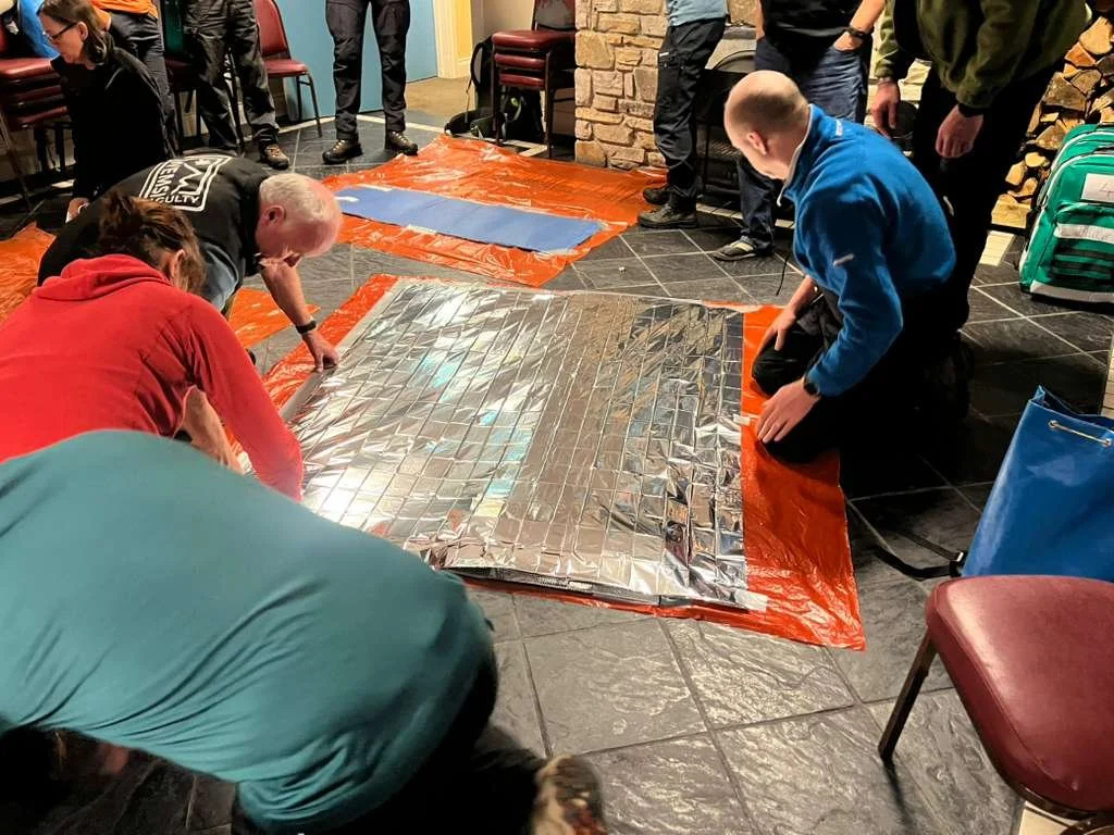 People gathered around a large solar panel placed on a tarp on the floor, some adjusting or inspecting it, in an indoor setting.