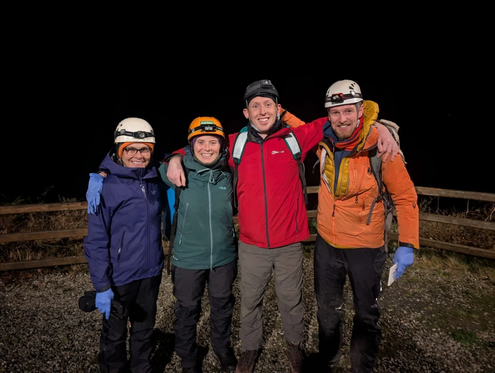 Group of five people in outdoor gear, smiling and posing with arms around each other at night.