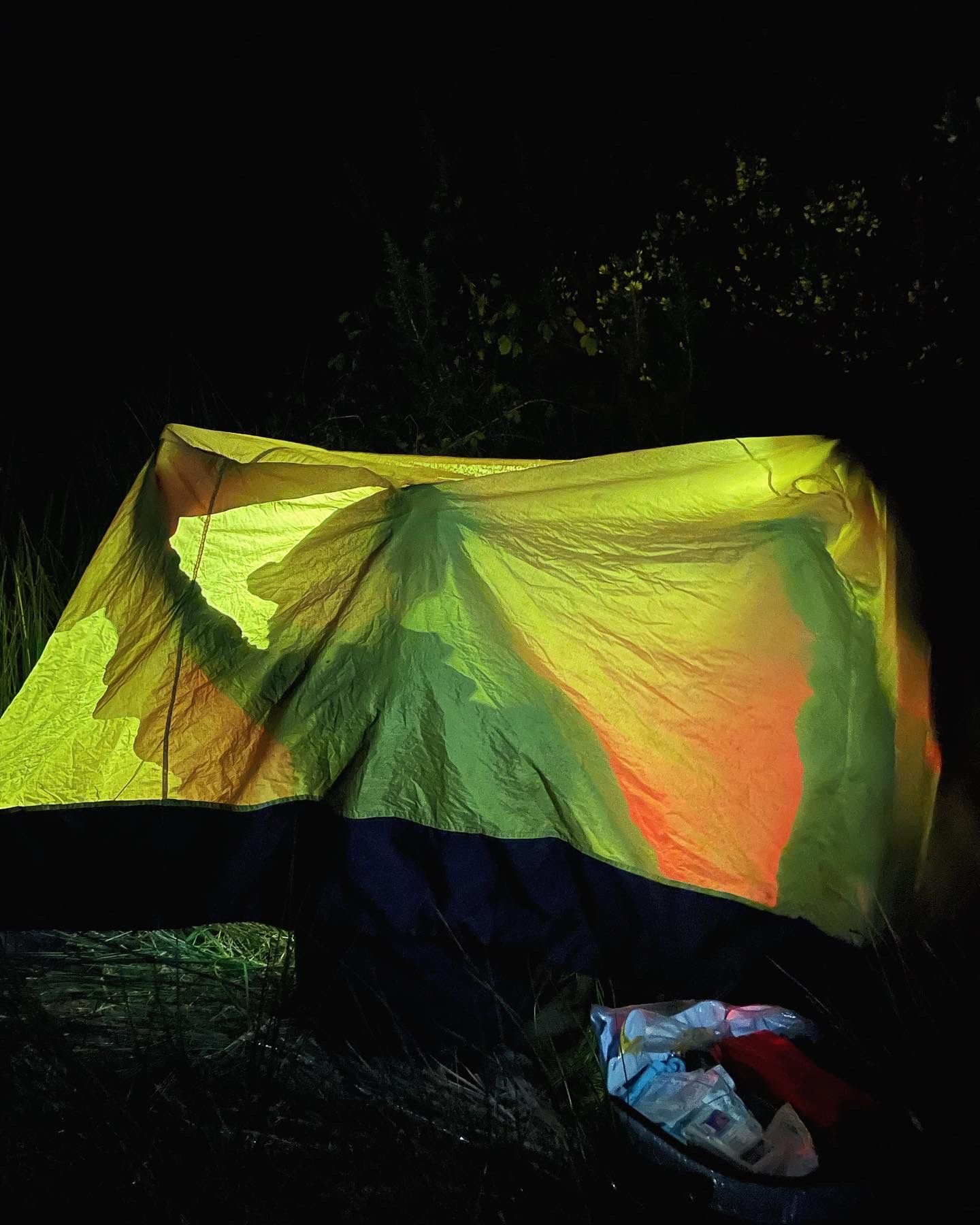 A dark outdoor scene showing a colorful, illuminated leaf-like fabric or tarp stretched out in the night, with some objects or supplies visible at the bottom.