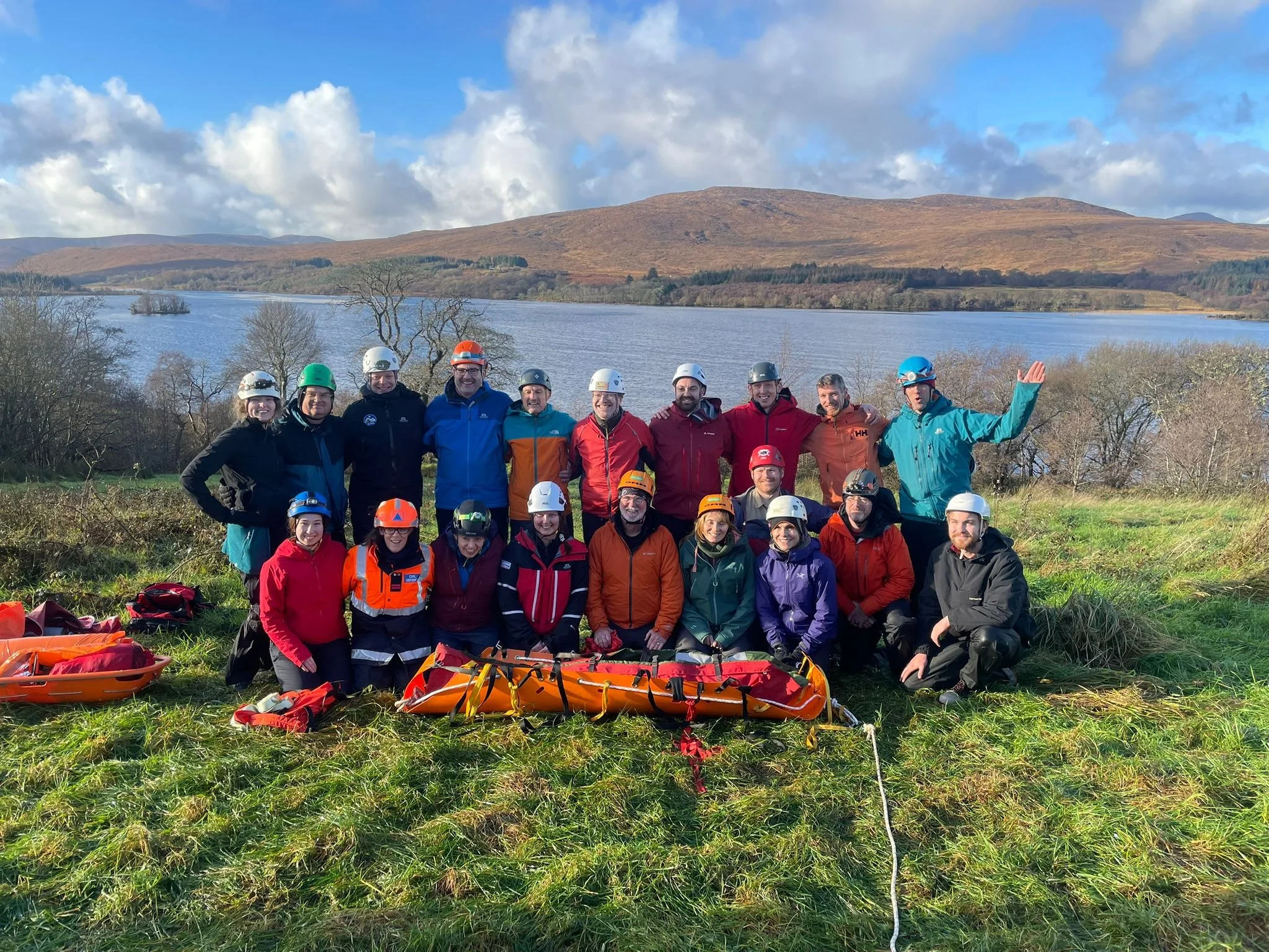 Group of people in rescue gear outdoors with water and hills in background.